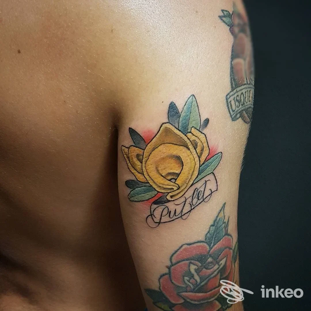 Tattoo floreale giallo con scritta corsiva sul braccio, colore vivace e contorni scuri, con un secondo tatuaggio rosso visibile in basso.