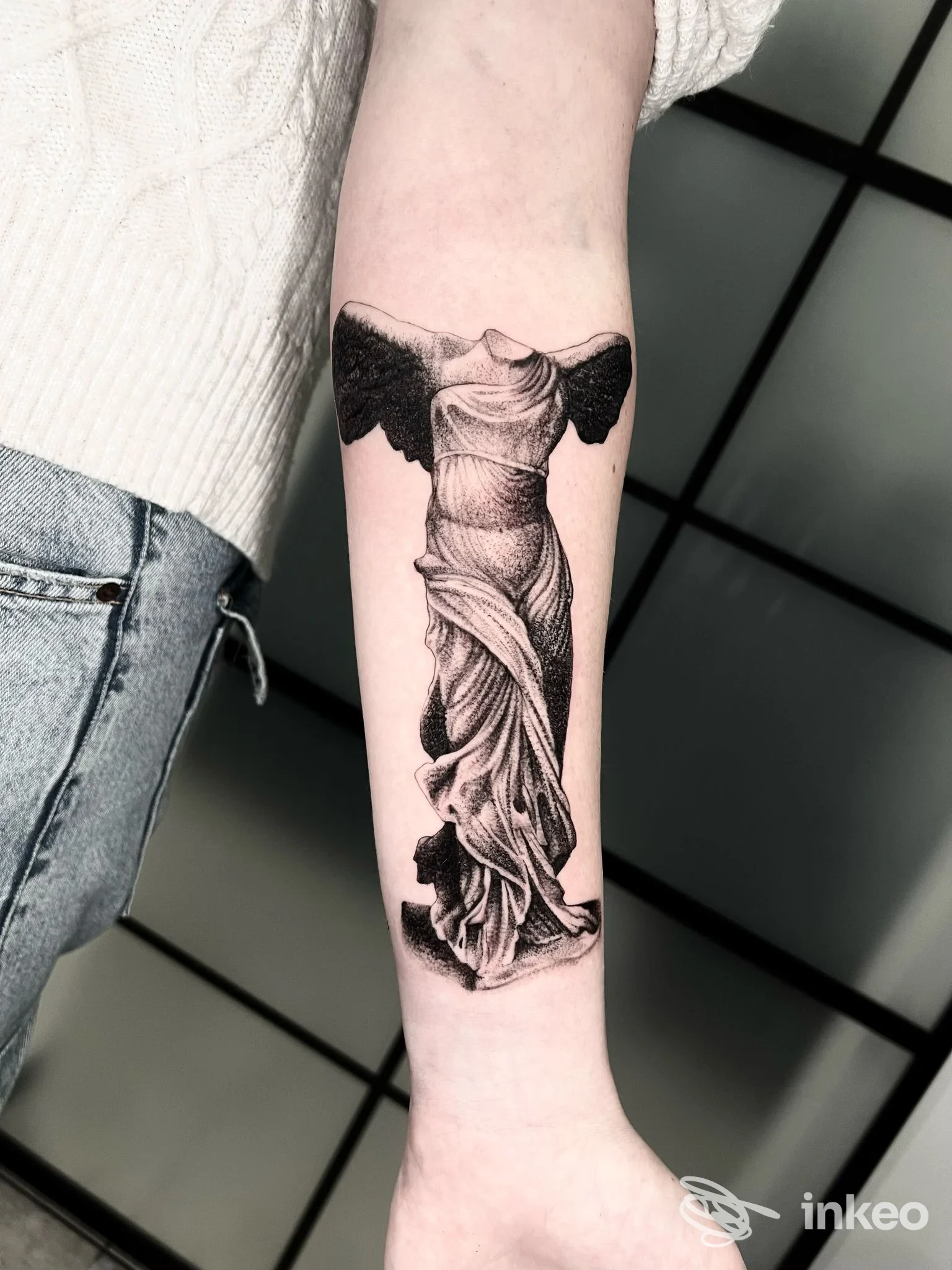 Tattoo realistico su avambraccio raffigurante una statua avvolta in drappeggio, realizzato sulla pelle e ben definito.