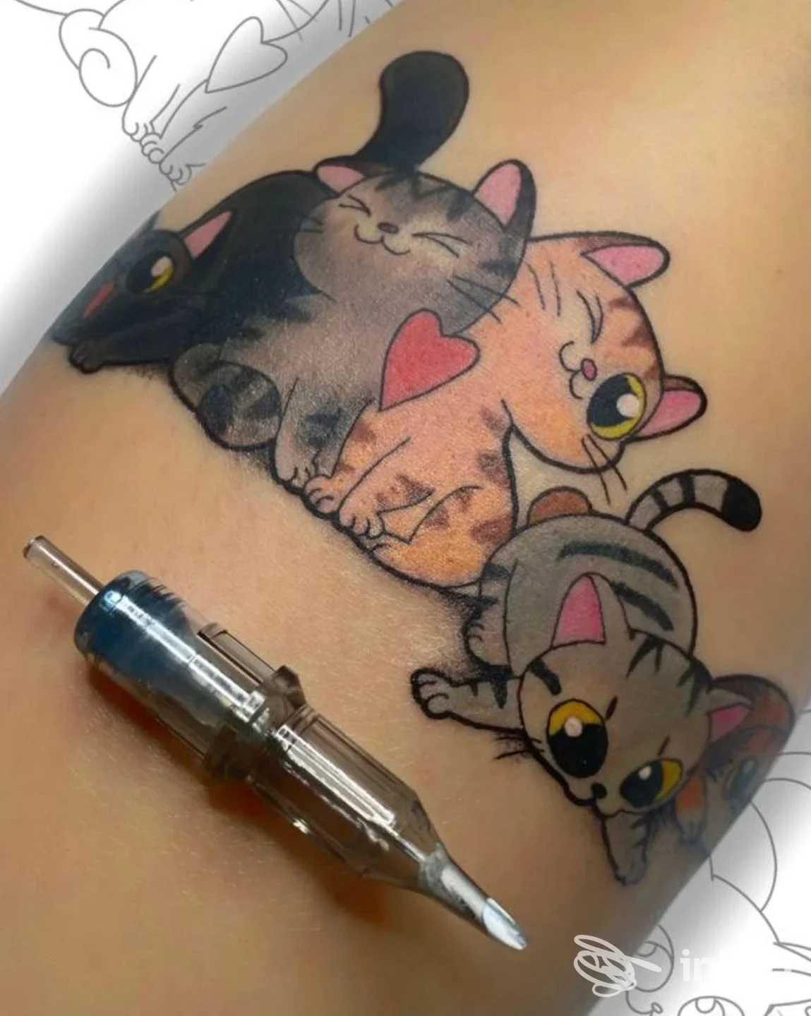 Tattoo colorato su pelle raffigurante tre gatti: nero, arancione e grigio, abbracciati, con penna da tatuaggio in primo piano.