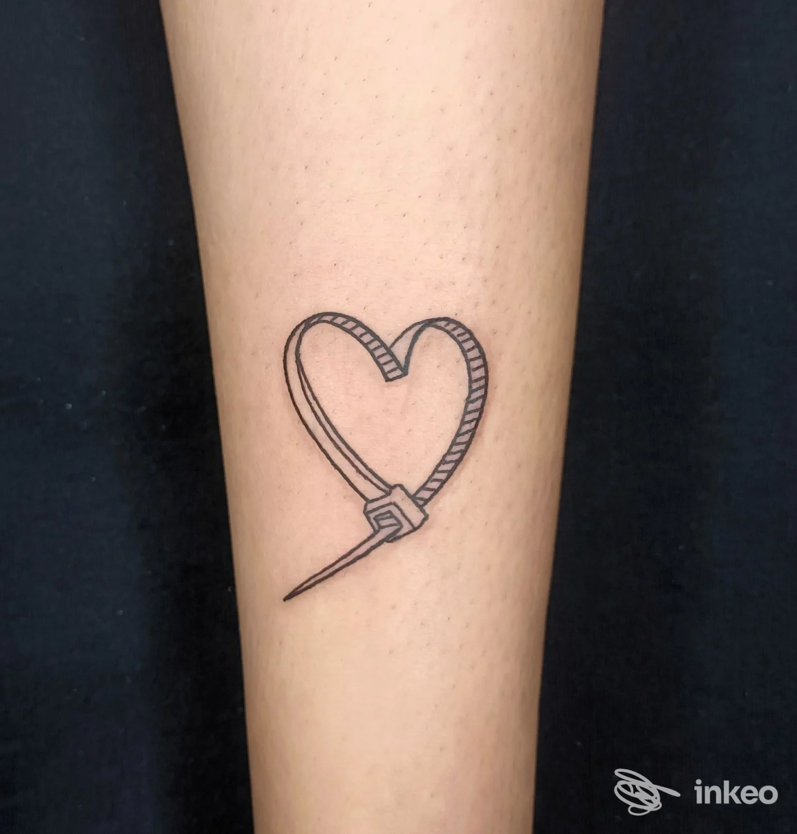 Tattoo su avambraccio raffigurante un cuore aperto con freccia, tratto nero pulito su pelle chiara.