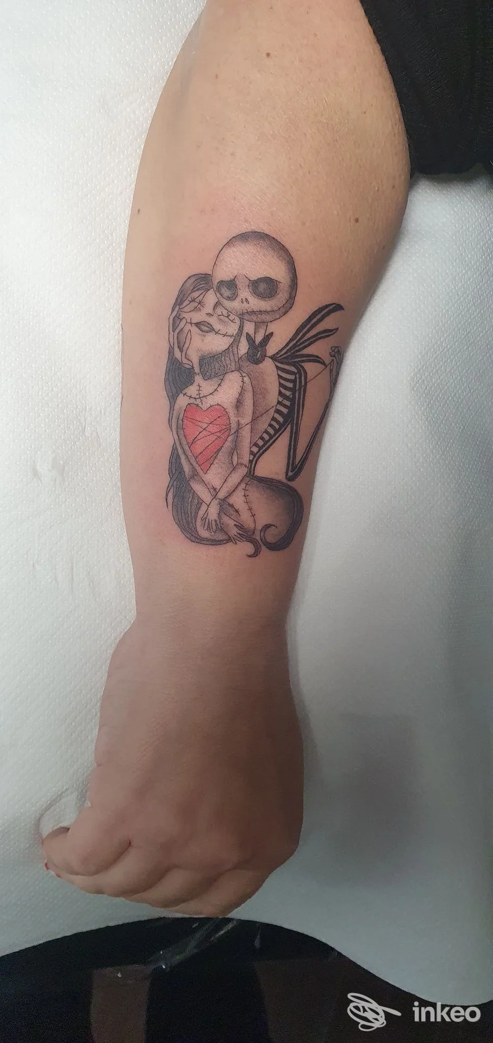 Tattoo sull'avambraccio: due scheletri abbracciati con cuore rosso, eseguito presso lo studio Helena.