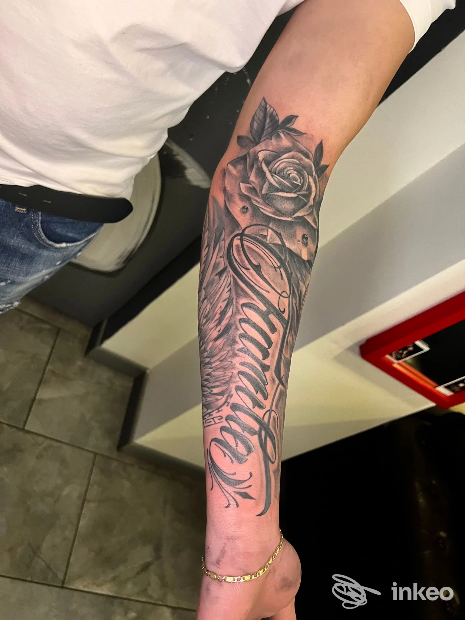 Braccio sinistro con tatuaggio realistico: rosa in alto e scritta corsiva sull’avambraccio, pelle visibile, nessun volto, senza watermark o testo promozionale. Studio Unique Arts Tattoo.