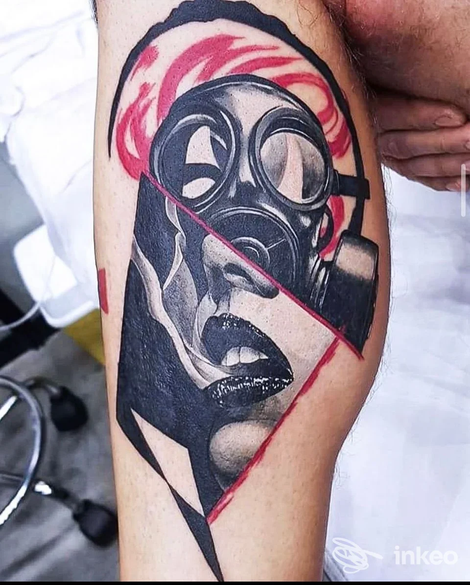 Tattoo realistico su pelle raffigurante una maschera antigas con sfondo rosso, visibile sulla gamba di una persona, senza volto inquadrato.