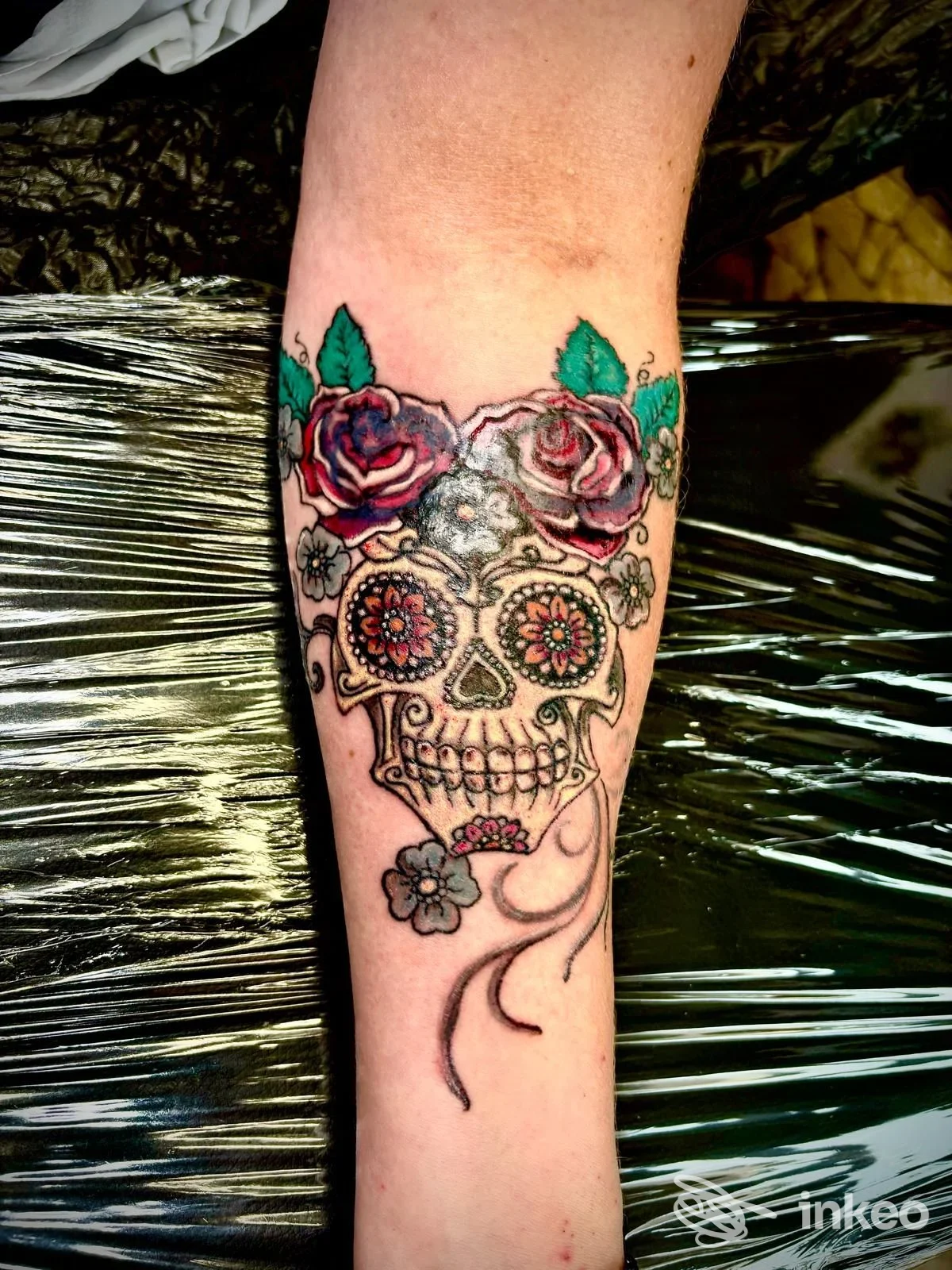 Tatuaggio sugar skull con rose sul braccio, linee nere marcate e colori vividi, visibile parte dell'avambraccio.