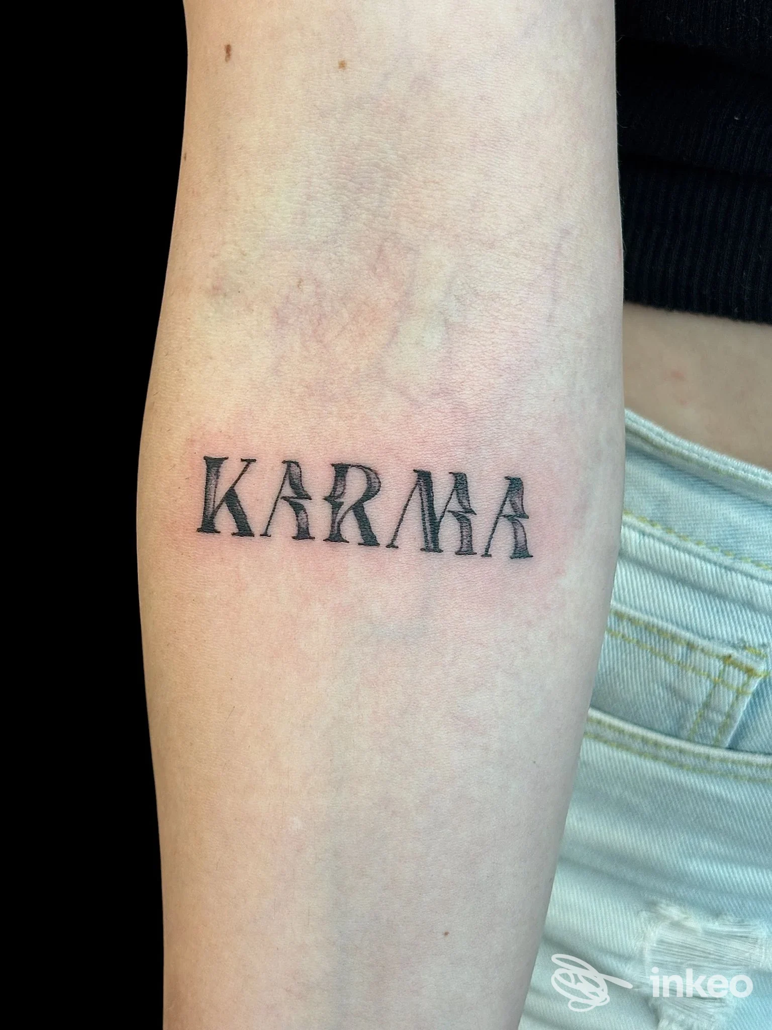 Tattoo su avambraccio raffigurante la parola KARMA in stile classico, visibile in una foto ravvicinata.