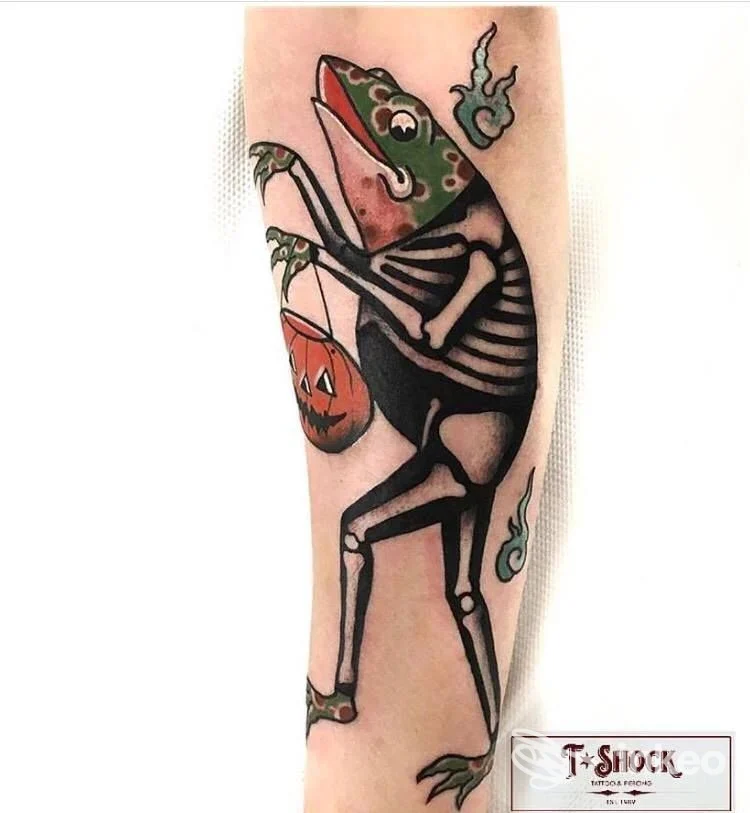 Tatuaggio su avambraccio di dinosauro scheletrico con secco e zucca di Halloween, contorni neri e colori vivaci, nessun volto visibile