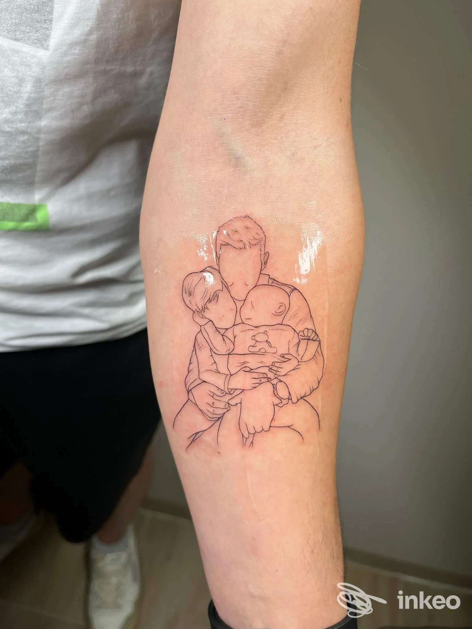 Tattoo su avambraccio raffigurante una famiglia in linee nere, disegno stilizzato di abbraccio tra adulti e bambini, visibile direttamente sulla pelle.