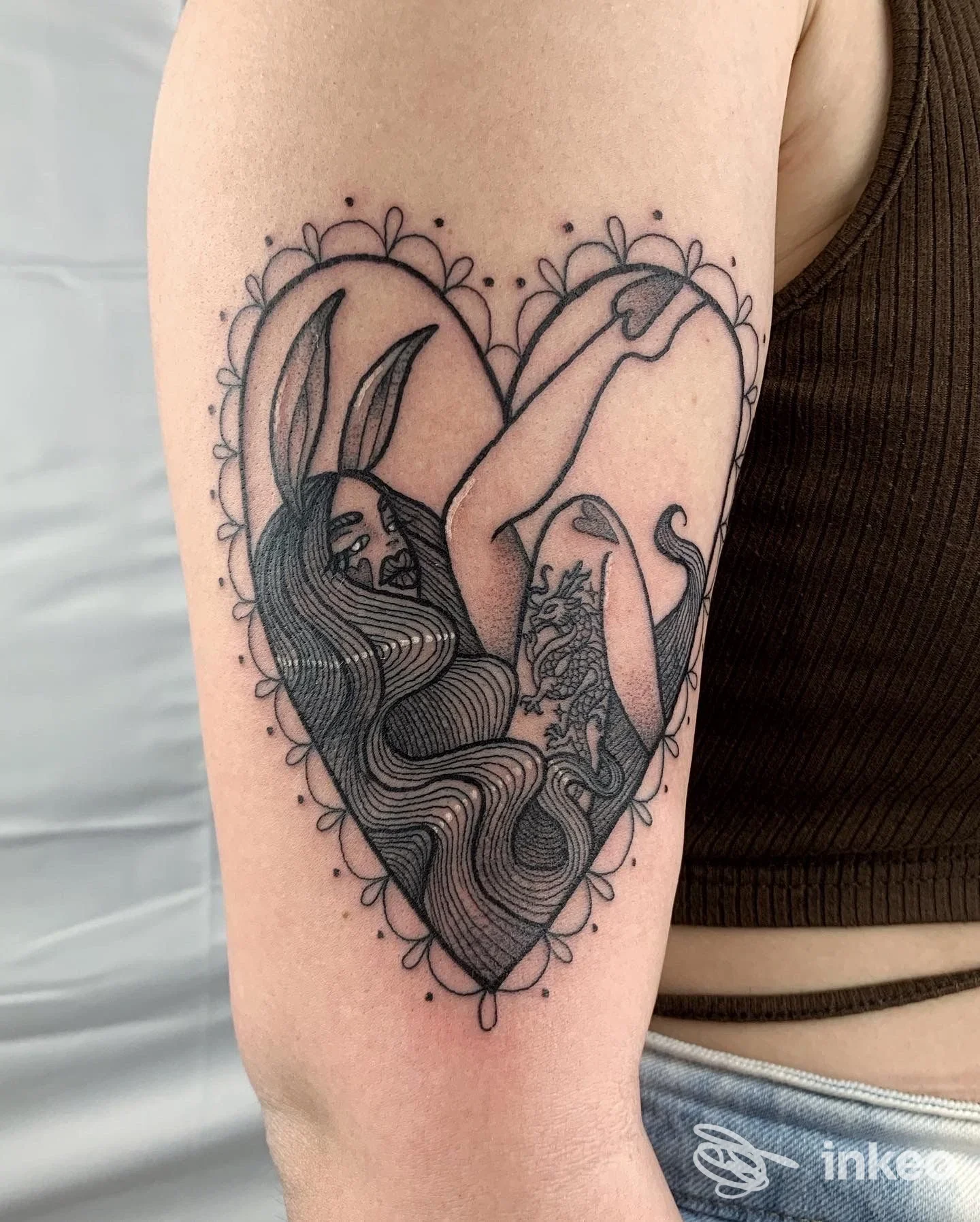 Tatuaggio sul braccio sinistro: cuore con una figura femminile dai capelli lunghi, contorno decorato, eseguito in stile linework.
