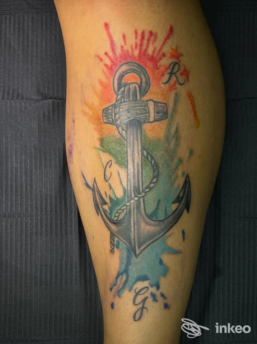 Tatuaggio ad anchor con corda e sfondo a schizzi colorati sull'avambraccio, senza volto visibile.
