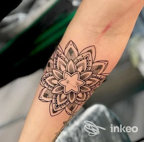 Tattoo mandala in bianco e nero sull’avambraccio sinistro, disegno linework preciso su pelle chiara, senza volto visibile.