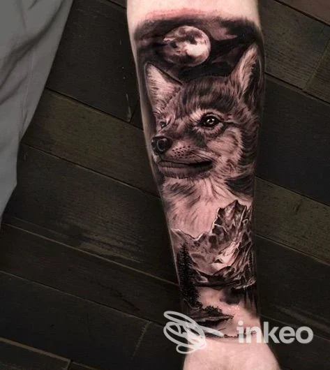 Tattoo in bianco e nero sull'avambraccio raffigurante una volpe con luna, accompagnata da paesaggio montano; nessun volto umano visibile.