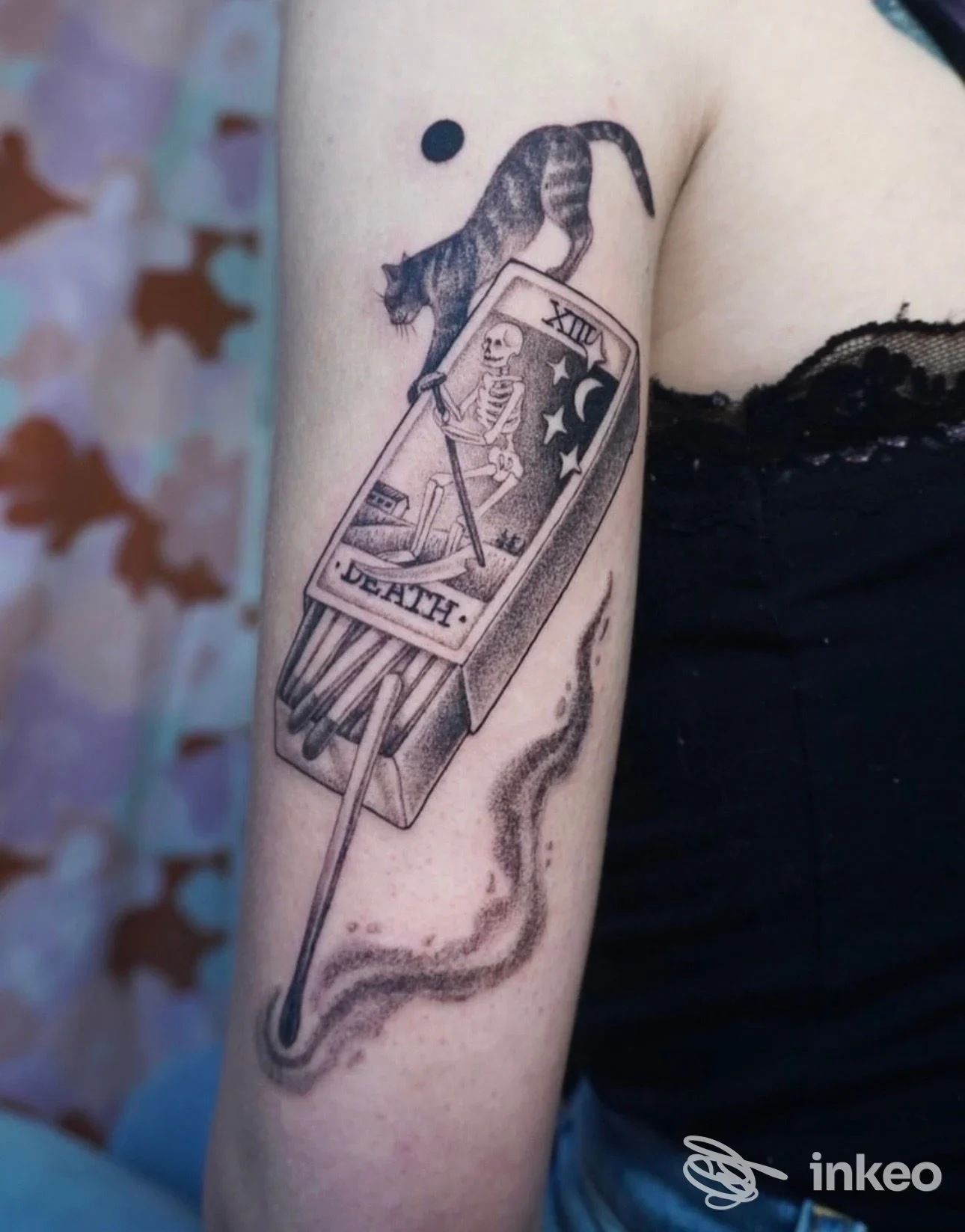 Tatuaggio su braccio raffigurante una carta di tarocco Death con figura scheletrica e un gatto sopra, eseguito in bianco e nero.