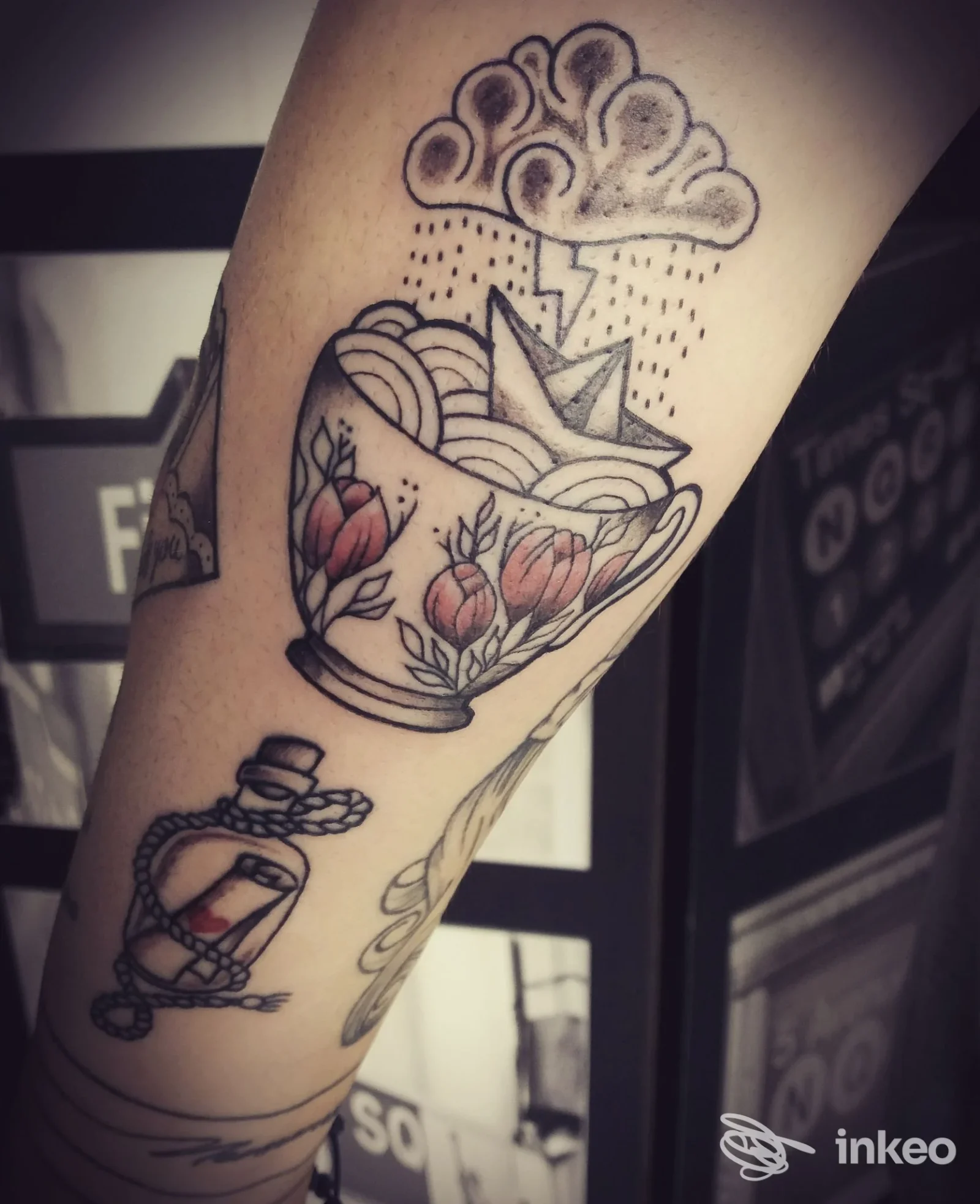 Tattoo sull’avambraccio raffigurante una tazza decorata con fiori e nuvole, con linee nette e sfumature scure; non si intravede volto umano.