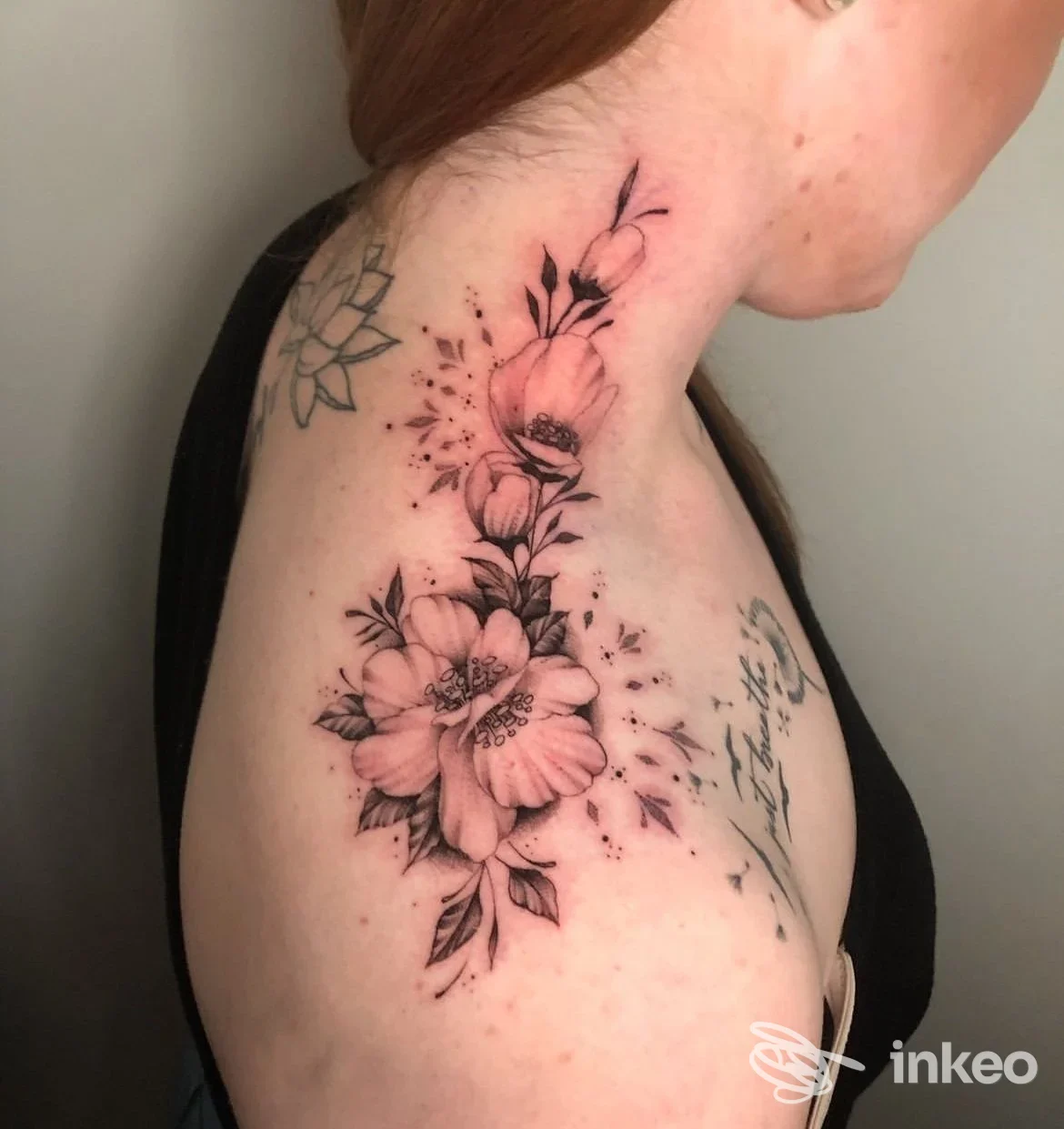 Tattoo floreale su spalla e braccio descritta con linee nette, ombre e dettagli floreali su pelle reale, realizzata in uno studio, con sfondo neutro.