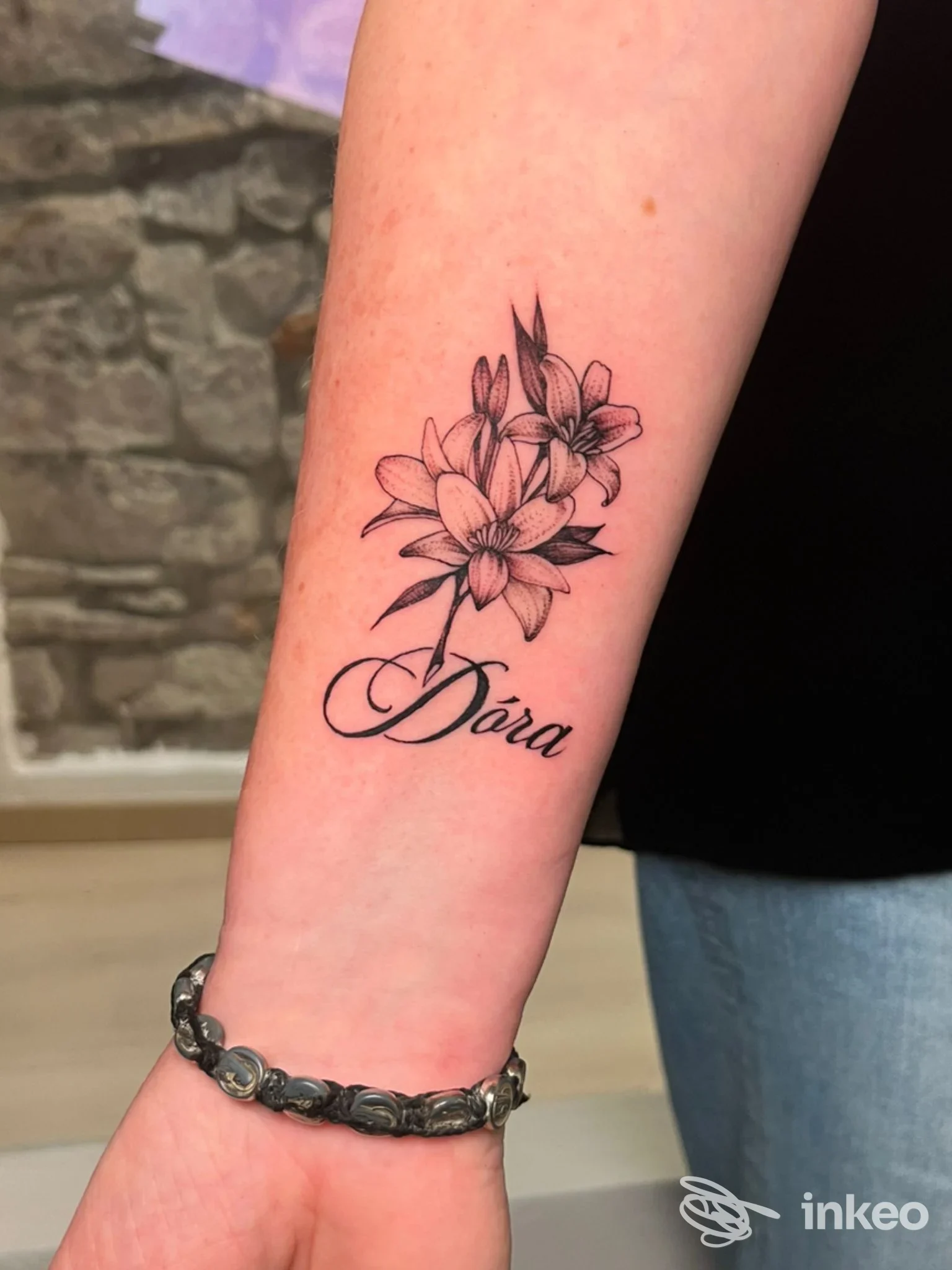 Tattoo floreale in inchiostro nero sull’avambraccio con scritta elegante: Dora. la pelle appare sana e non vi sono elementi esterni visibili.