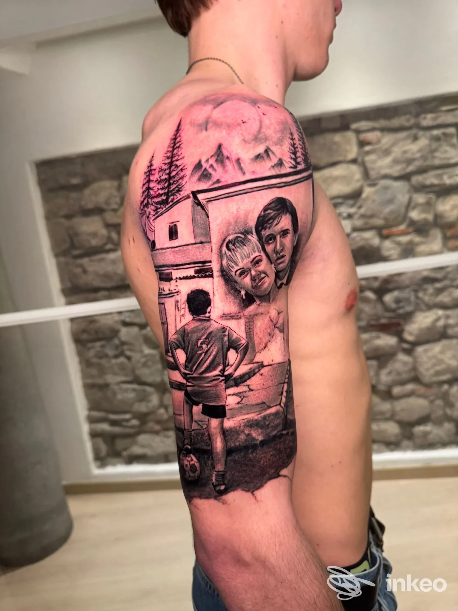 Tattoo realistico sul braccio di un uomo: paesaggio montano con alberi e edificio, affiancato da ritratti di due persone; eseguito nello studio Iseo Tattoo Studio.