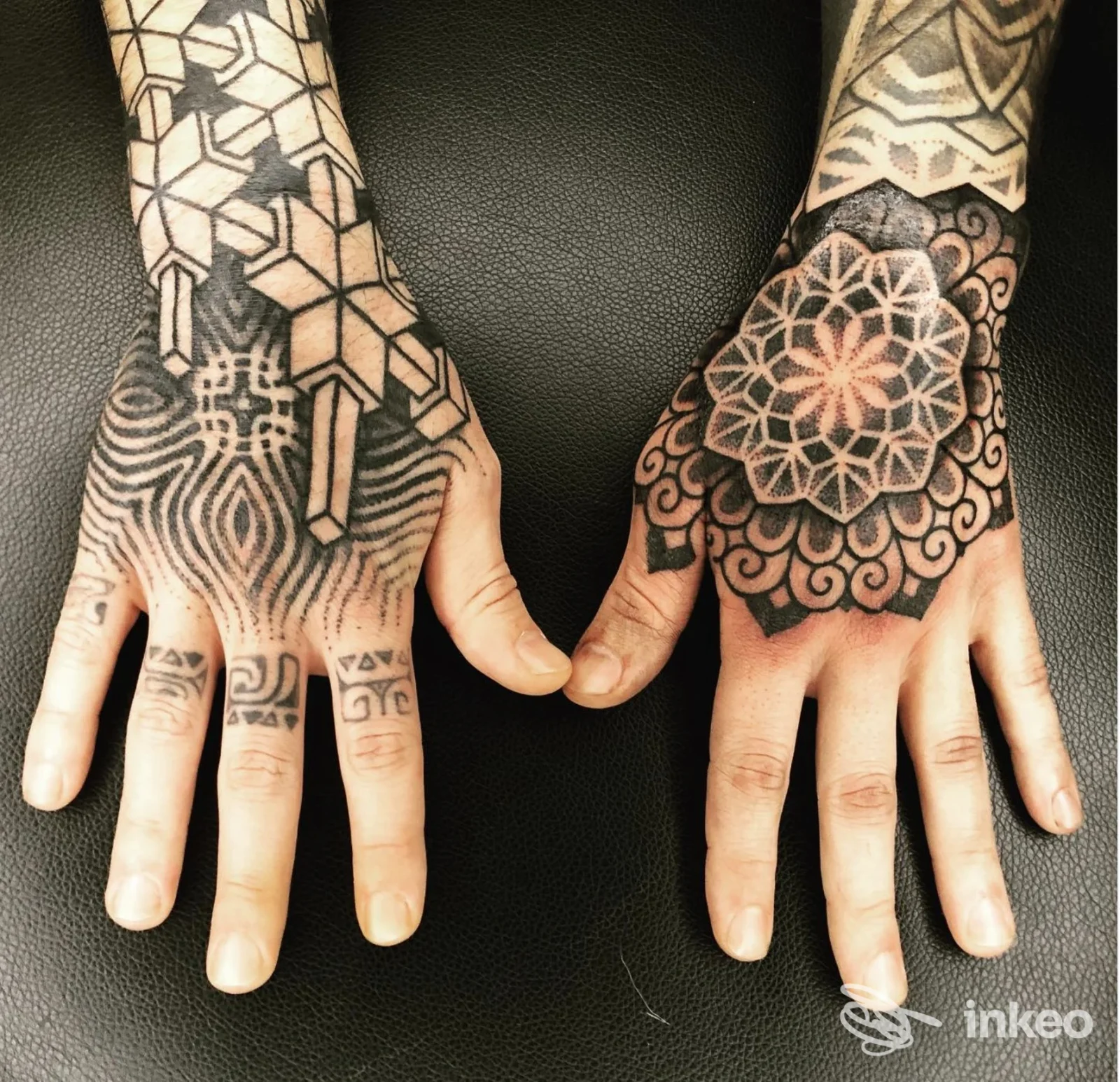 Due maniche con tattoo neri su dorso e dita, motivo geometrico e mandala, scatto ingrandito su pelle reale, nessun volto visibile, stile tatuaggio.
