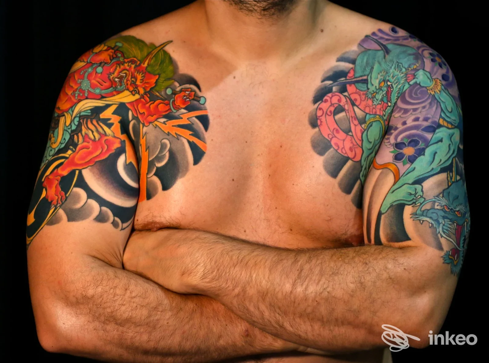 Torace e braccia di un uomo, completamente tatuati a colori vividi con motivi dinamici, in posa di braccia incrociate.