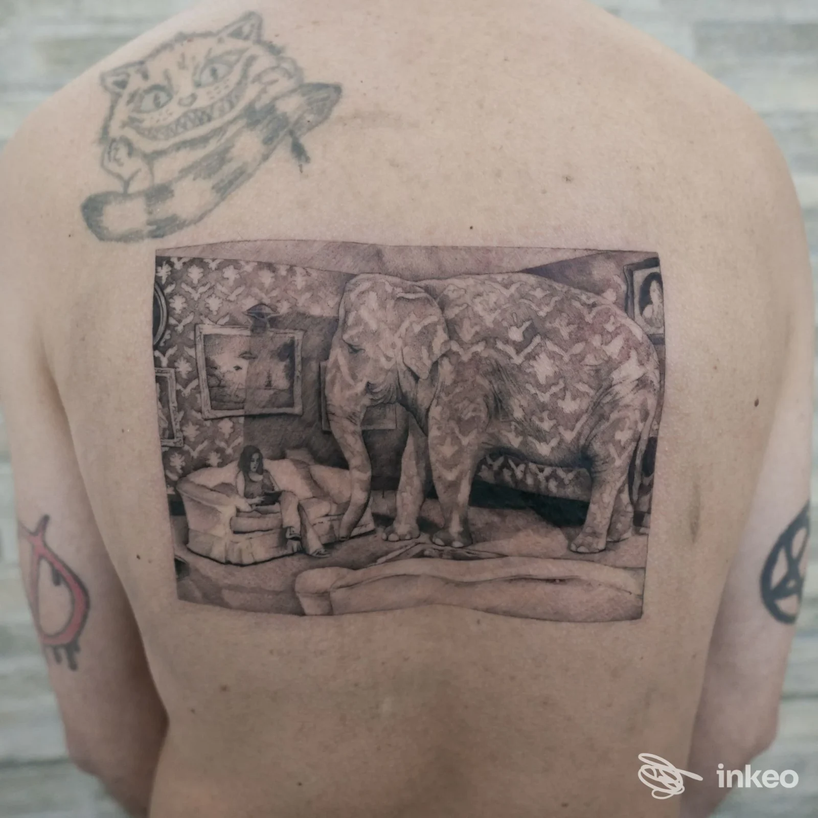 Tattoo sul dorso raffigurante una scena interna con elefanti in una cornice rettangolare, presente su pelle nuda, accompagnato da altri tatuaggi sulle spalle.