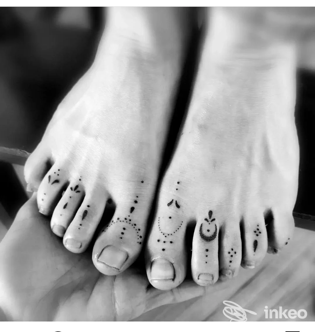 Piedi con piccoli tattoo sulle dita, disegni neri visibili sulle dita dei piedi, senza volto o testi visibili, scatto in bianco e nero.