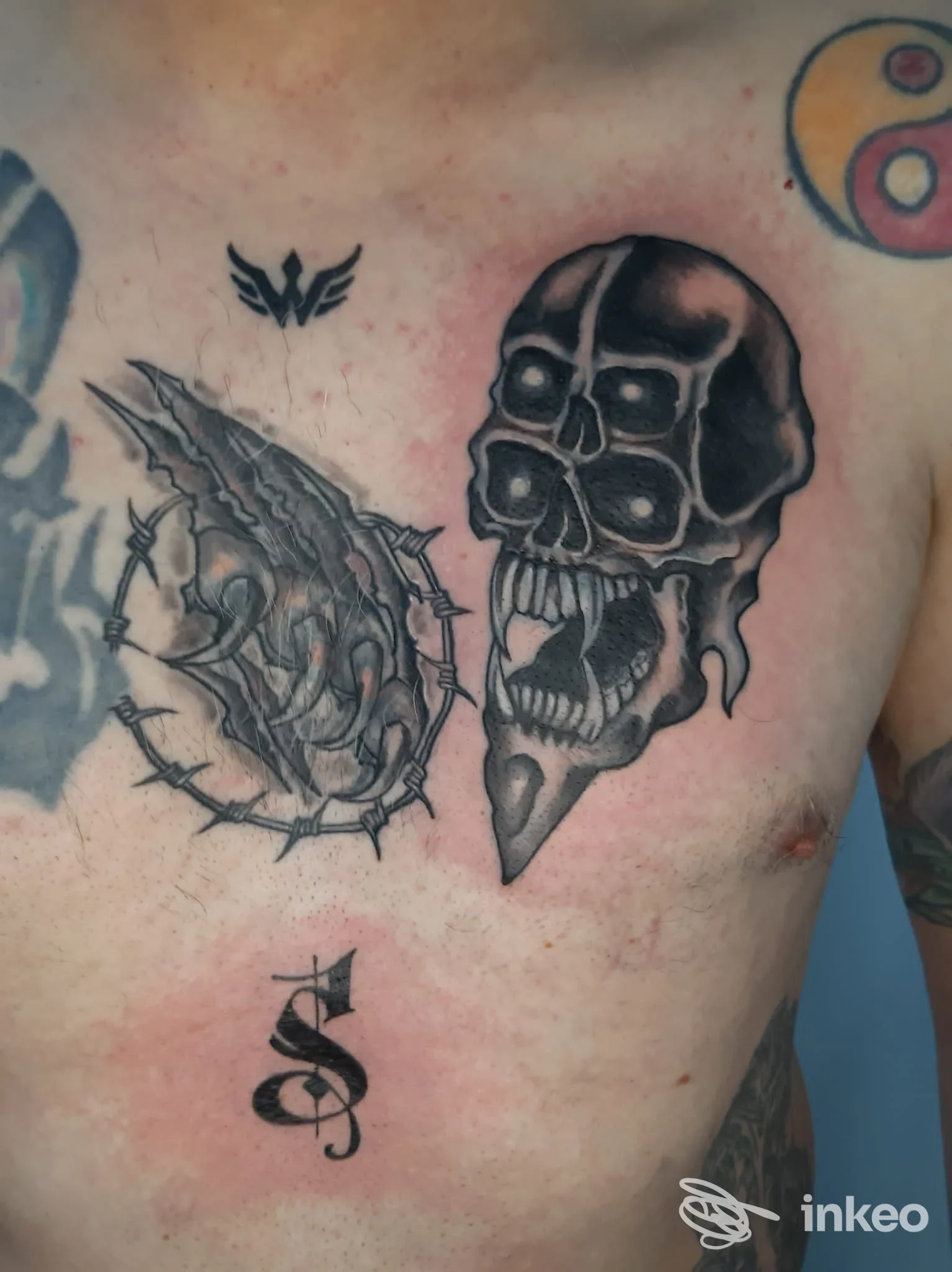 Tattoo sul torace: una testa di teschio scuro e una figura con elementi spigolosi sono visibili sulla pelle; scatto di torace di una persona con una parte superiore del busto; contenuto esterno a fini di marketing non presente, promosso dallo studio Kosmos.