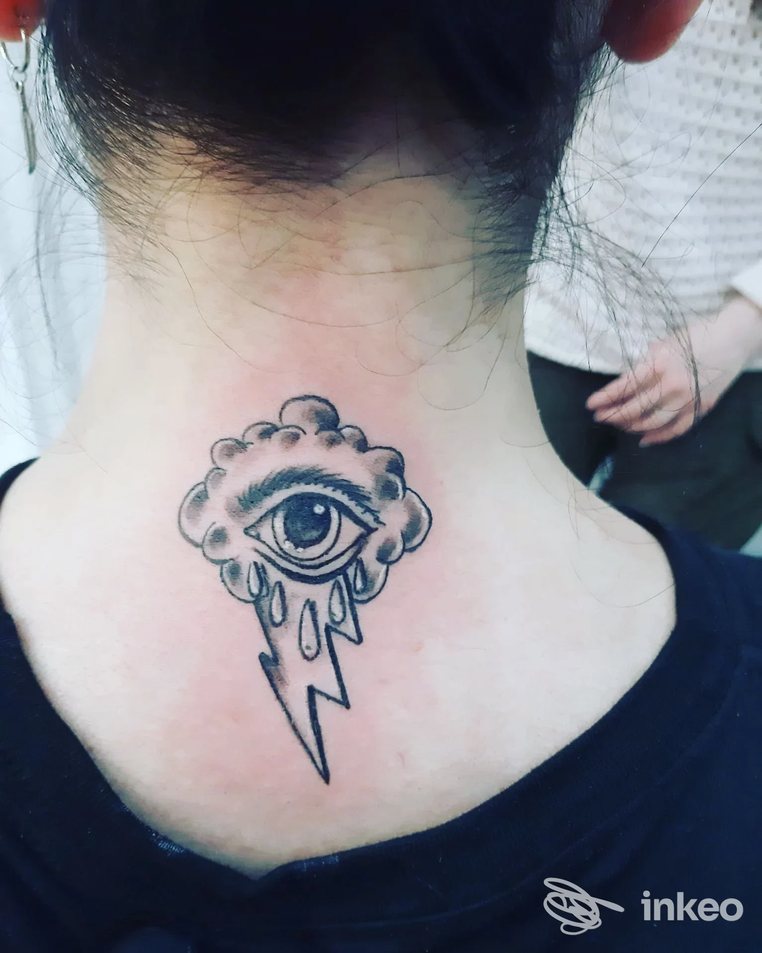 Tattoo reale sul collo posteriore: occhio dentro una nuvola, gocce e una freccia/fulmine, eseguito sulla pelle umana. L’immagine non mostra facce intere né contenuti di social media.