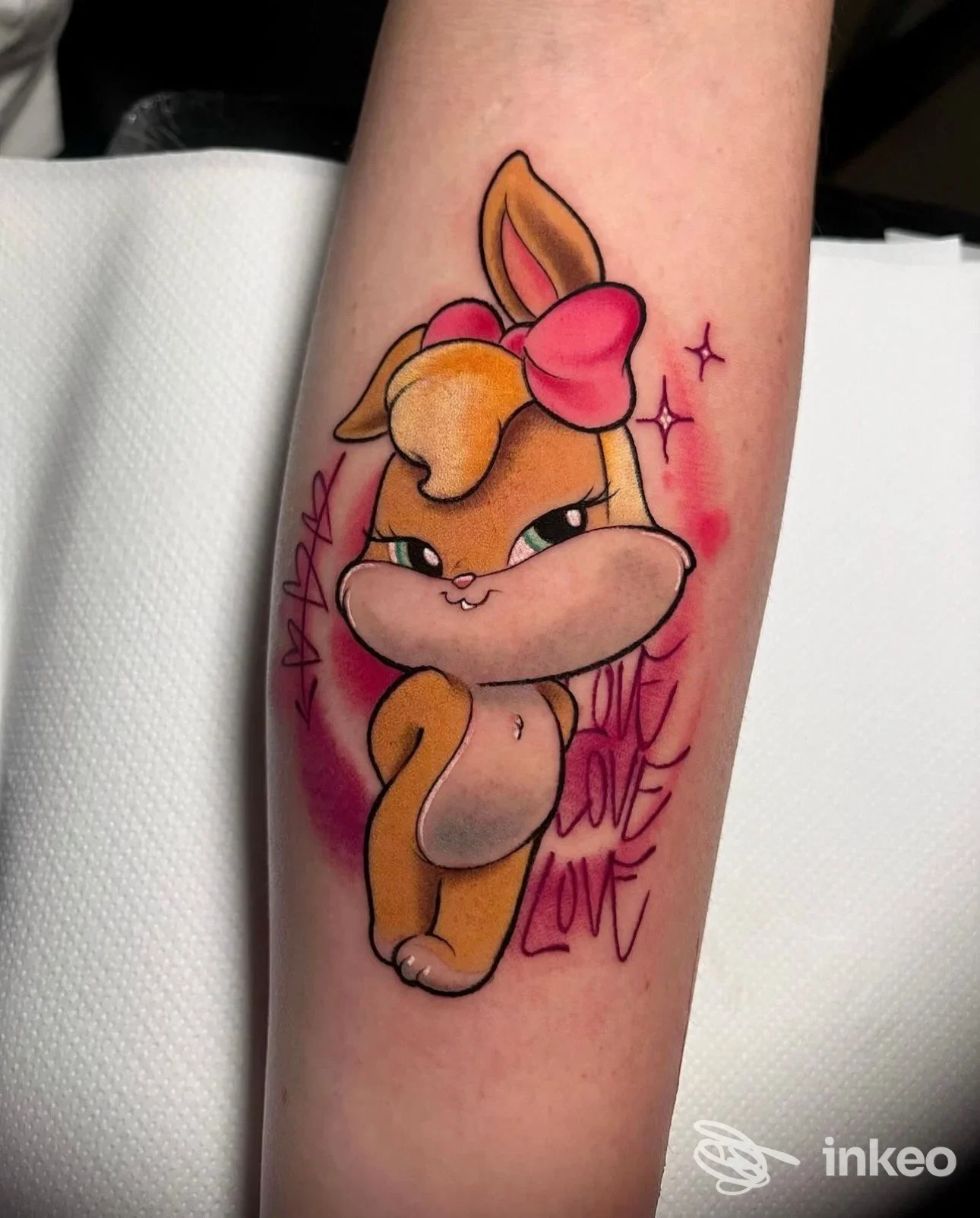 Tattoo su avambraccio di un coniglietto cartoonesco colorato con fiocco rosa. colori vivaci e contorni neri.