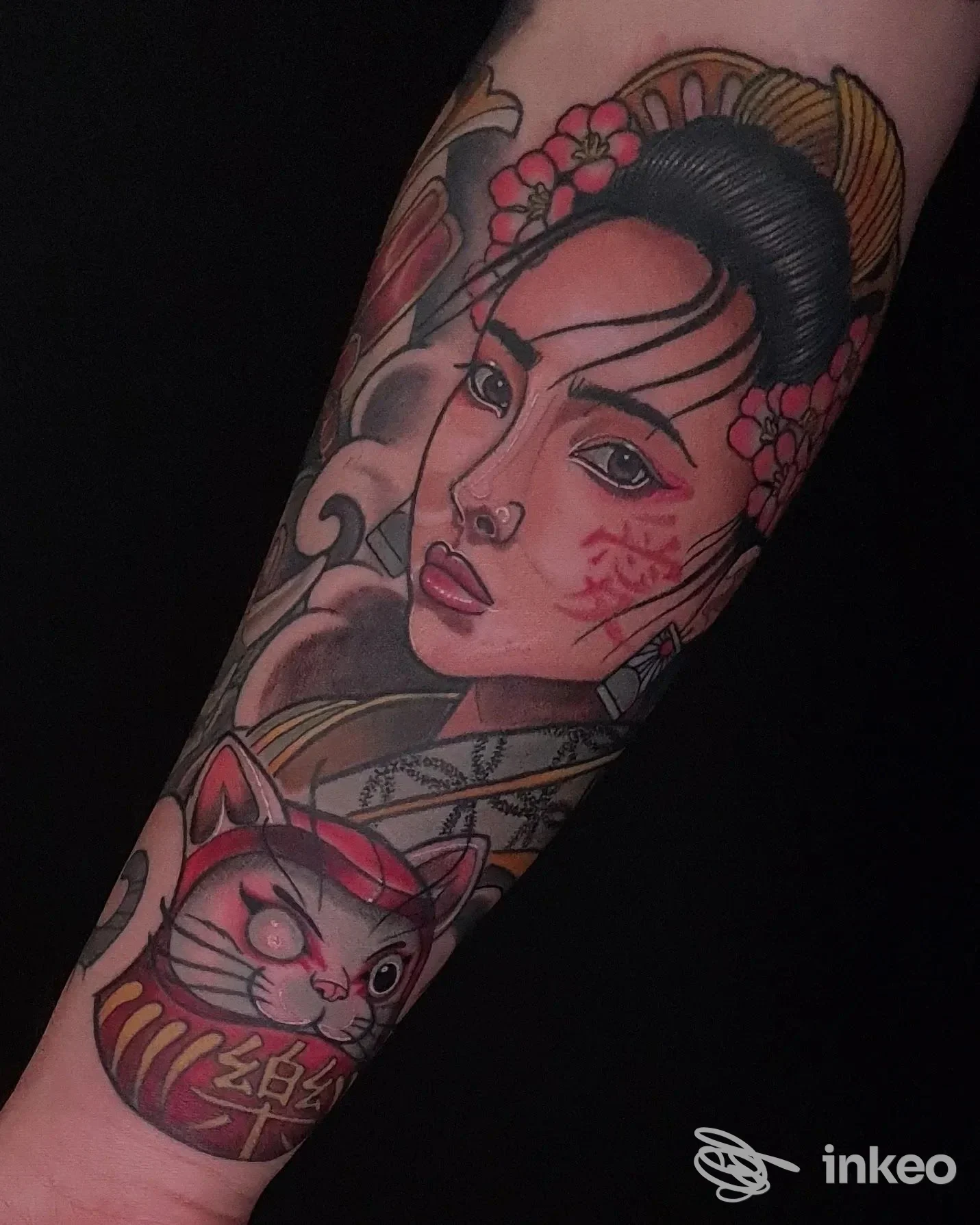 Tatuaggio completo su avambraccio raffigurante una geisha stilizzata con fiori e un gatto Maneki-neko in stile giapponese, su pelle chiara.