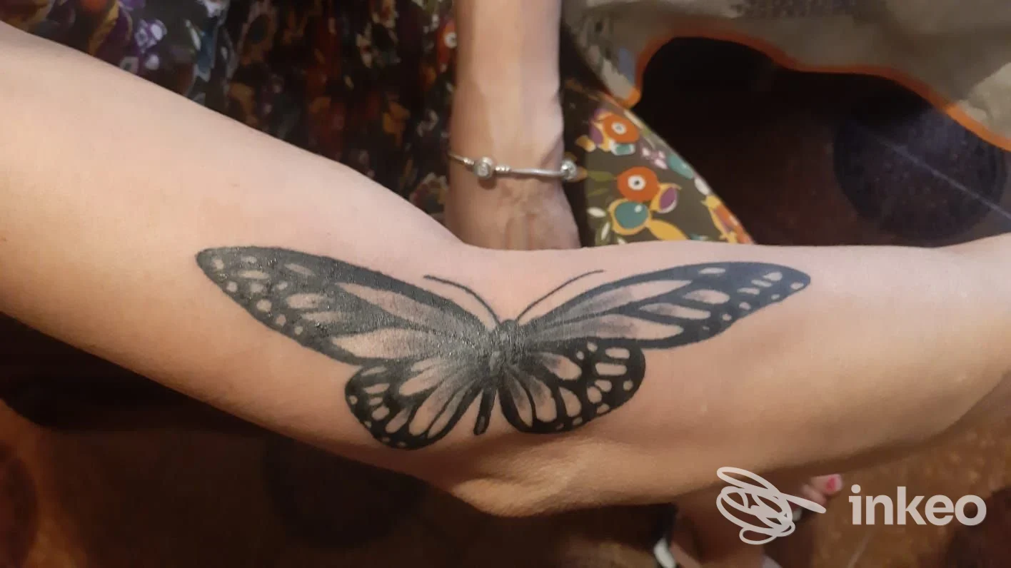 Tattoo su avambraccio: farfalla stilizzata nera visibile su pelle di una persona, senza visi o elementi estranei, foto centrata sull'avambraccio.