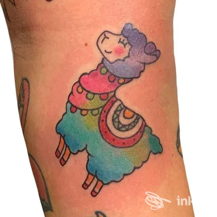 Tattoo a colori su pelle raffigurante una lama alpaca stilizzata, con sciarpa colorata, visibile sul braccio.
