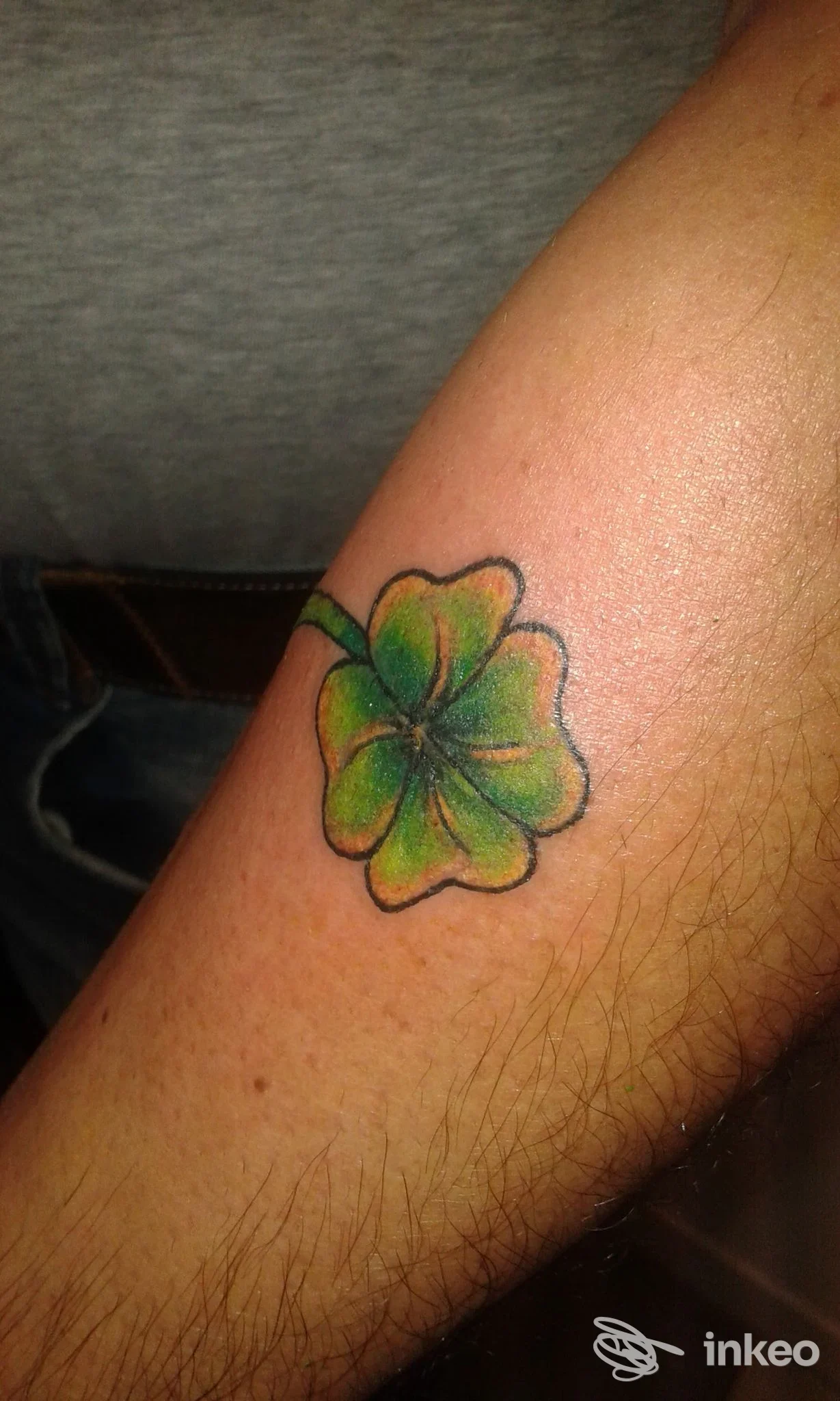 Tatuaggio colorato a fiore verde su pelle di avambraccio; disegno netto, contorni scuri, senza altri elementi visibili.