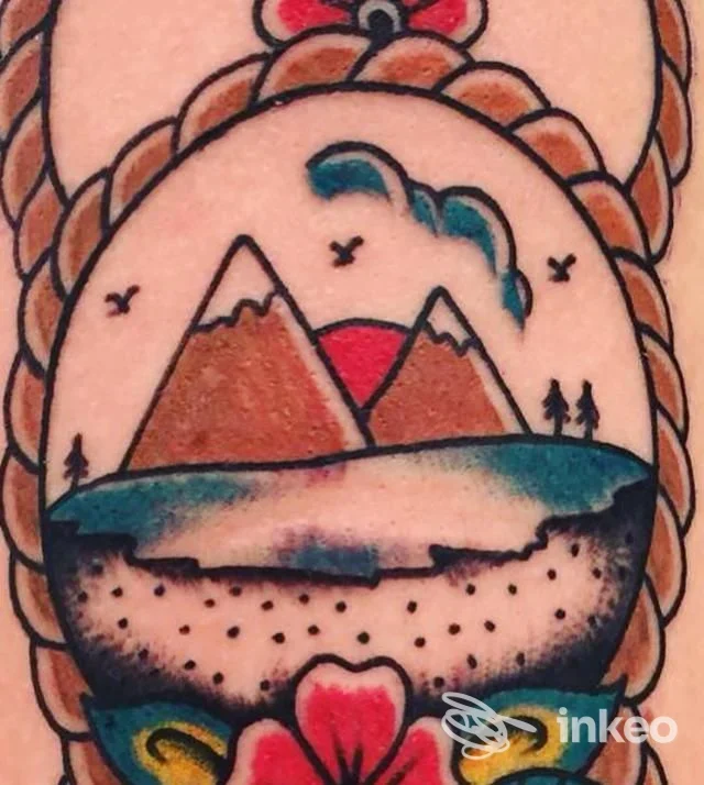 Tattoo visibile su pelle con paesaggio montano, lago e cielo, contorni neri netti e colori vivaci; primo piano di braccio.