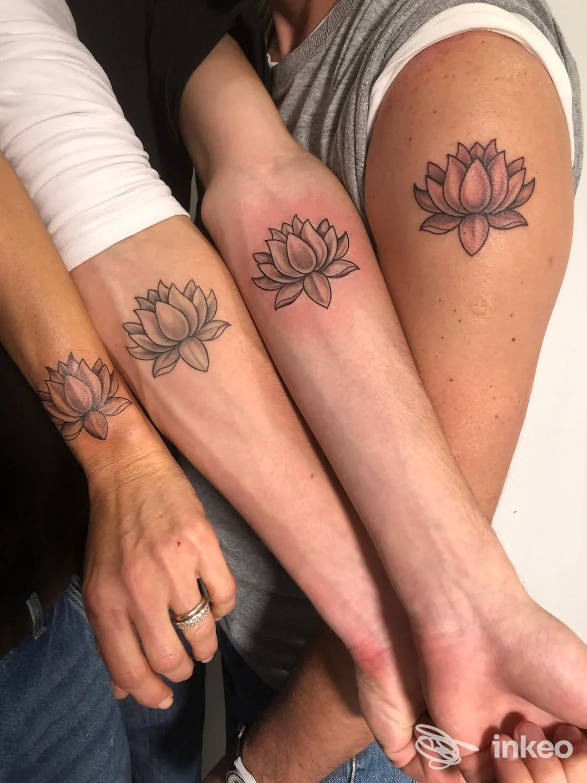 Avambracci di quattro persone, ciascuno con un tatuaggio a lotus sul braccio, visibili frontalmente in un riquadro unico.