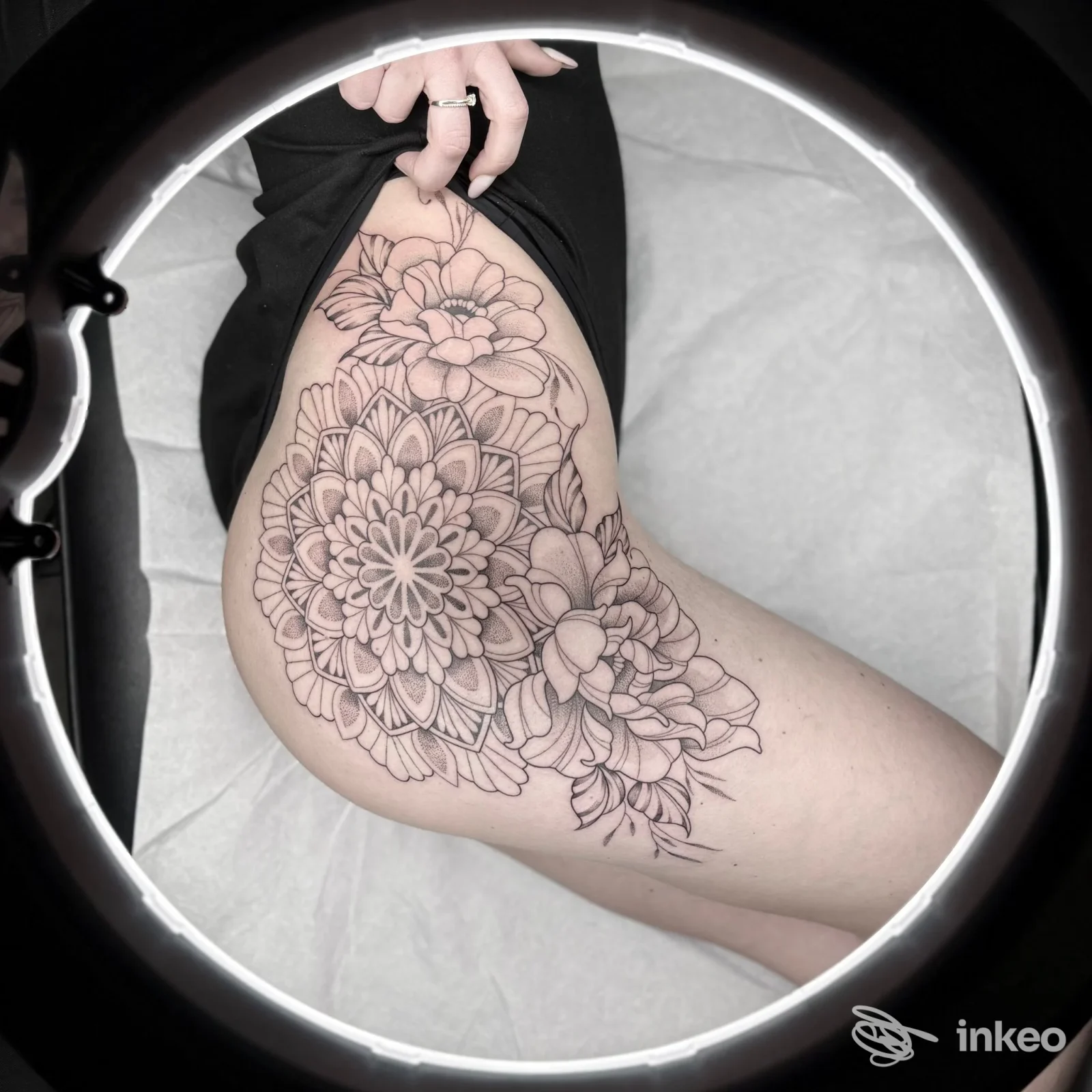 Tattoo floreale molto dettagliato sulla coscia sinistra, realizzato direttamente sulla pelle; è visibile solo il braccio e la gamba senza volto, tatuaggio primario. Studio Pamela Poma Ink.
