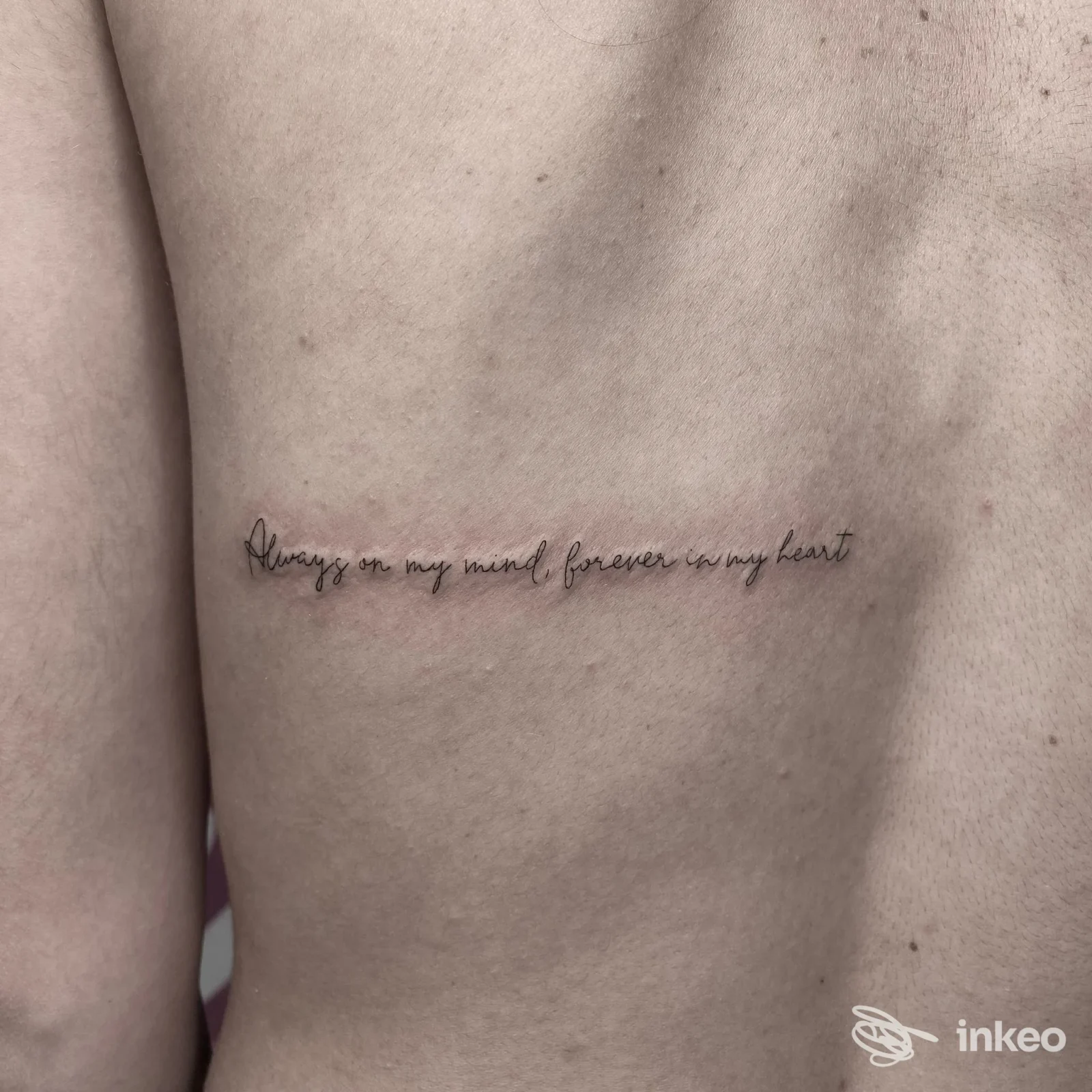 Tattoo testuale in corsivo sulla pelle della schiena, viste da dietro, senza visione del volto.