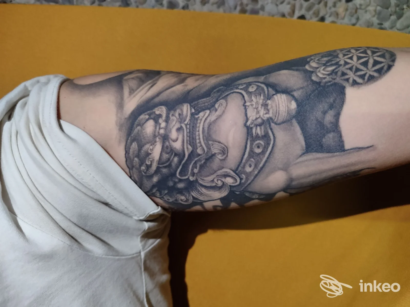 Braccio adulto con grande tatuaggio in tonalità grigio/nero su pelle, visibile davanti a sfondo giallo, scatto laterale; studio COR MEUM Tattoo di Gavirate.