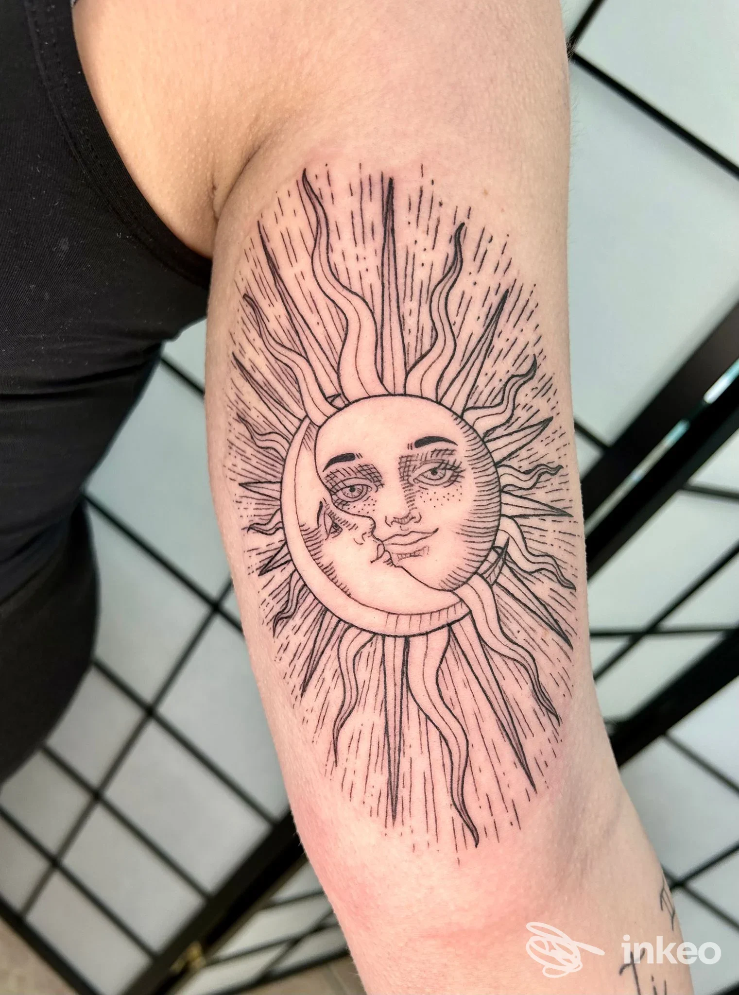 Tatuaggio sull'avambraccio raffigurante una luna con volto e raggi solari, in stile linework, realizzato sulla pelle reale.