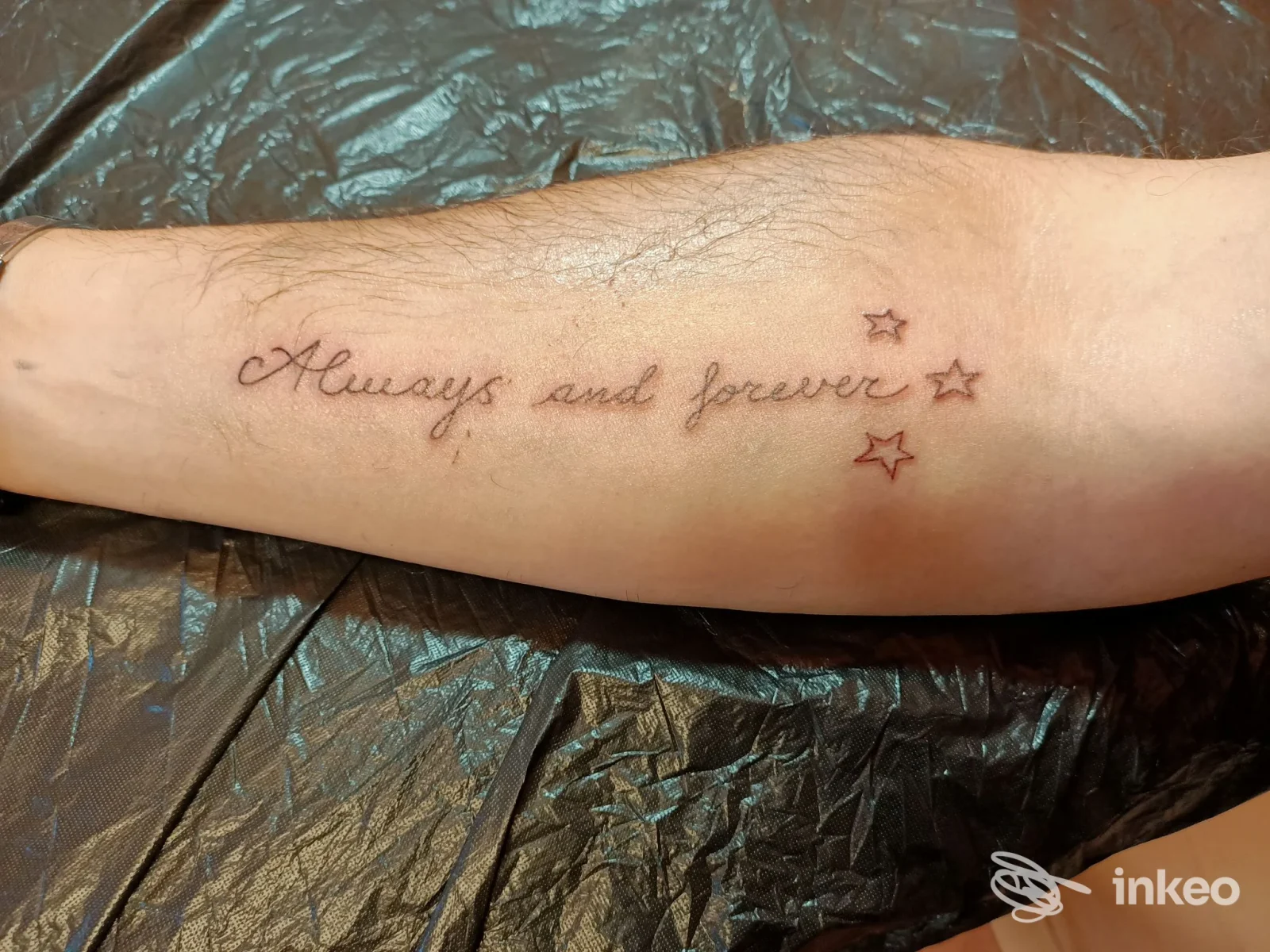 Avambraccio con tatuaggio di testo corsivo "Always and forever" accompagnato da piccole stelle, realizzato sulla pelle.