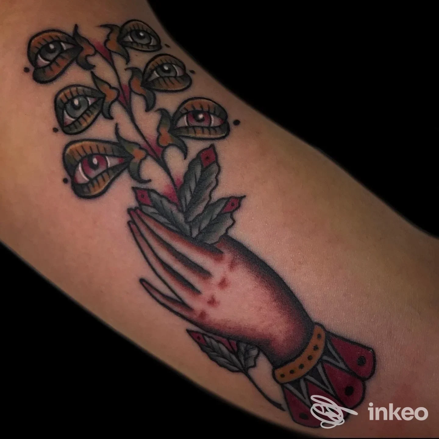 Tattoo sull'avambraccio raffigurante una mano stilizzata con dita allungate e rami di occhi, colorata in stile tradizionale.