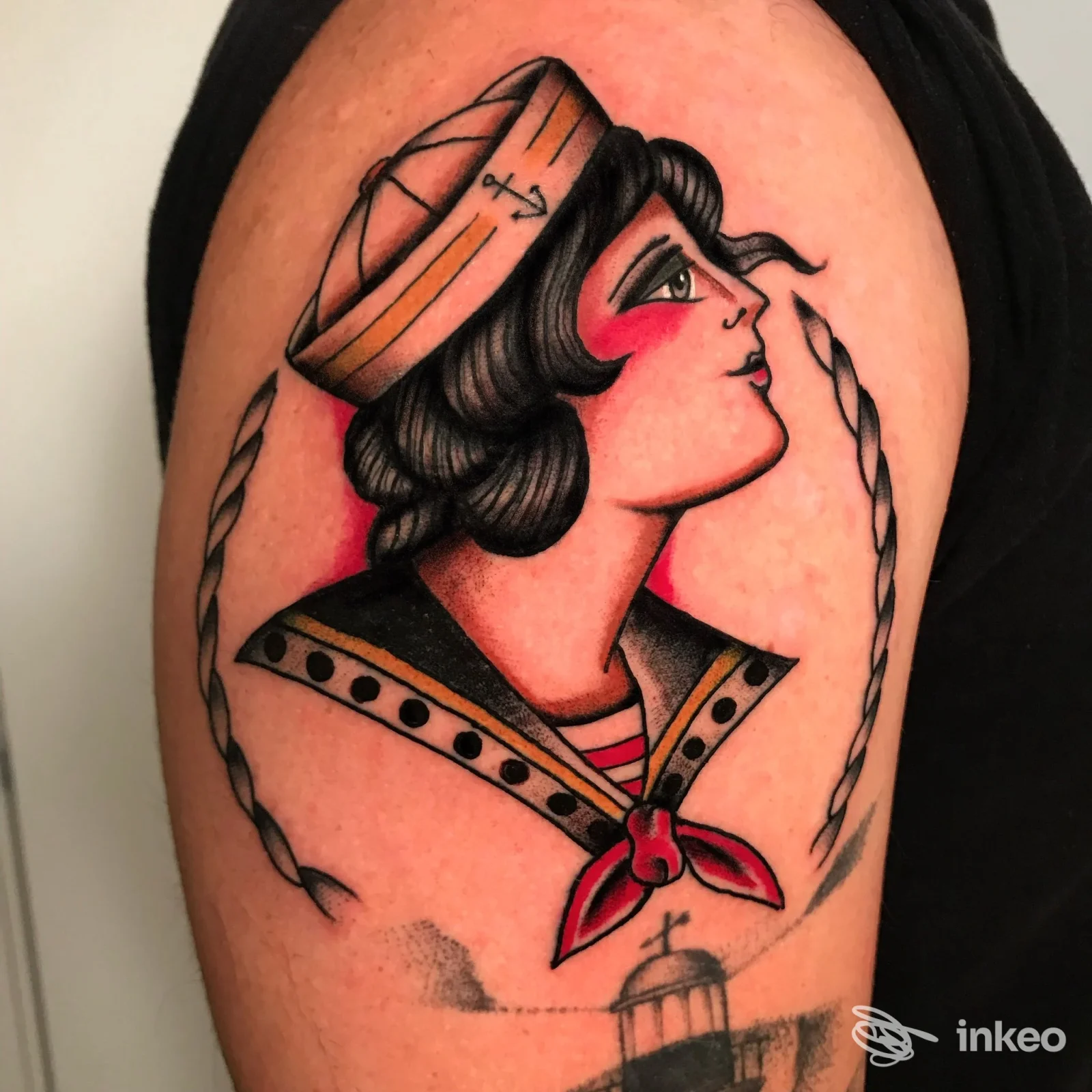 Tattoo sul braccio raffigurante una giovane marinaia, cappello e una corda, con tonalità rosse e dorate, realizzata sulla pelle.