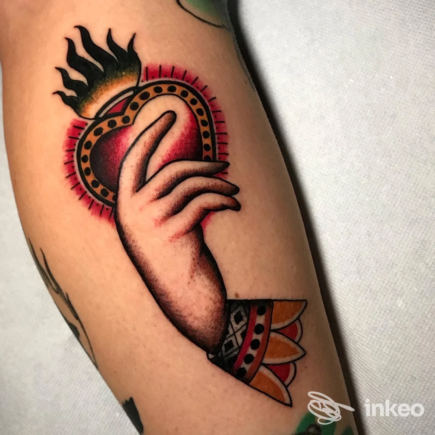Tattoo sul braccio raffigurante un cuore con mani e fuoco, colori vividi e contorni definiti.