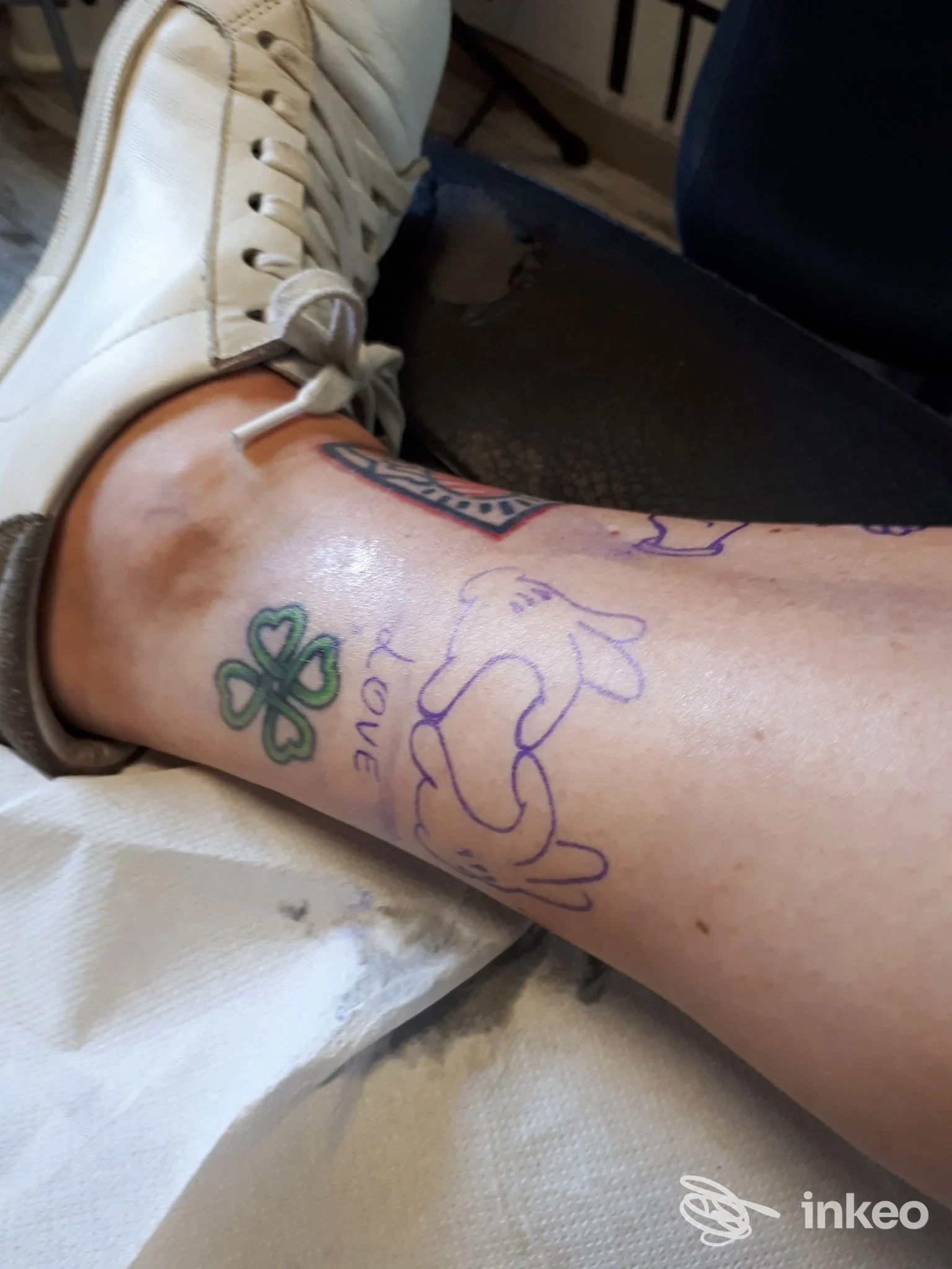 Dispositivo visibile: caviglia con piccolo tattoo verde a quattro foglie, assieme a schizzi viola temporanei e una sneaker bianca. appare una zona di pelle con disegno reale e schizzi in corso, studio Gia Tattoo, Seregno.