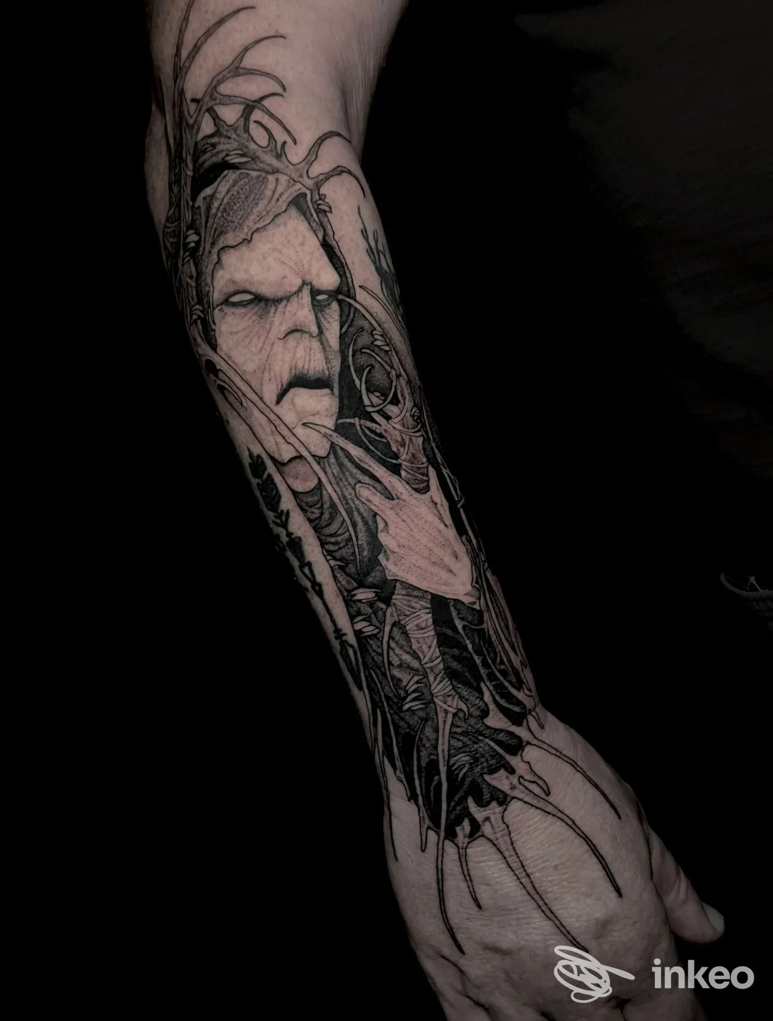 Tattoo sul braccio raffigurante una figura stilizzata in bianco e nero su sfondo scuro, visibile dal polso al mezzo avambraccio, con linee sottili e shading dettagliato.