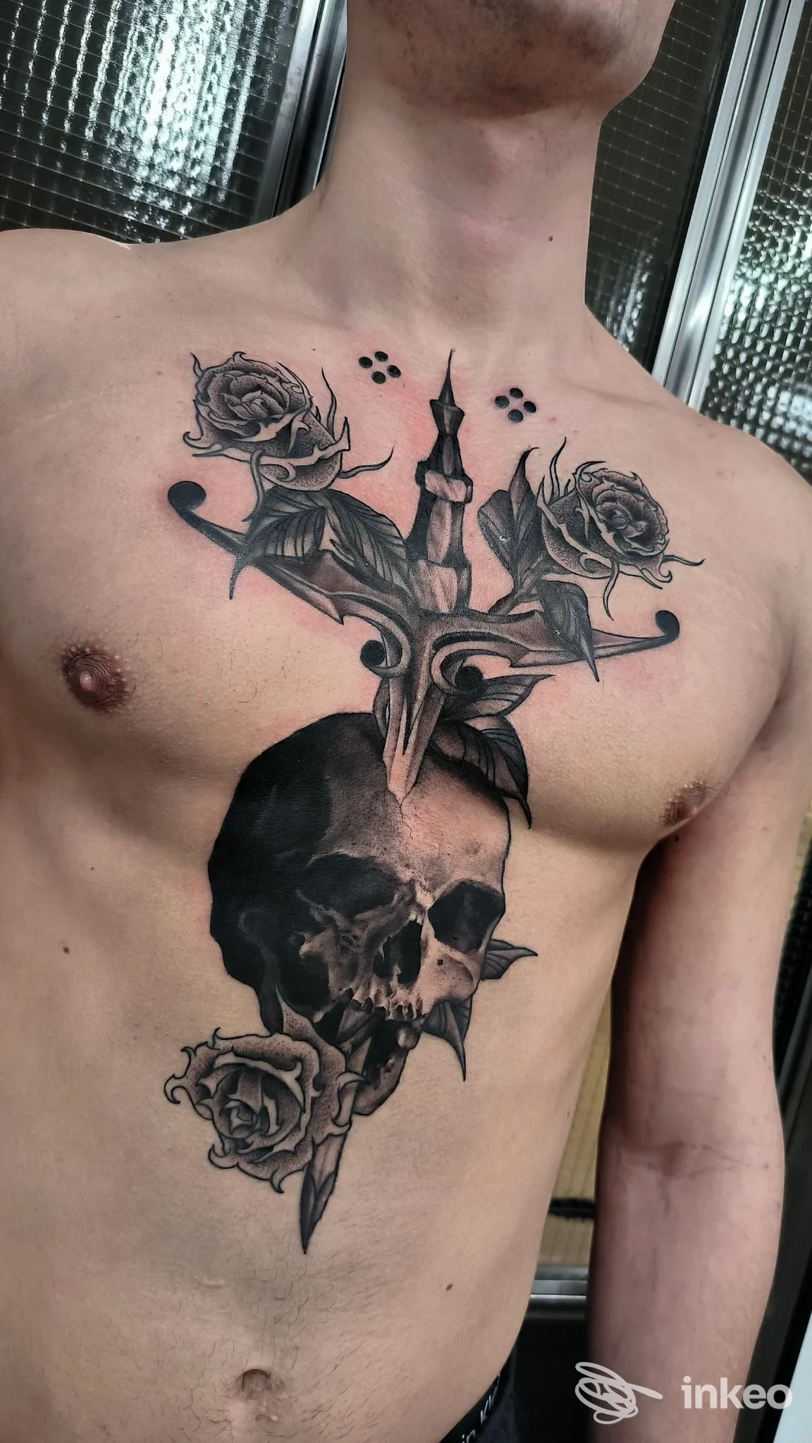 Tatuaggio sul torace di un teschio con spada e rose ai lati, realizzato sulla pelle umana, visibile nella zona del petto.