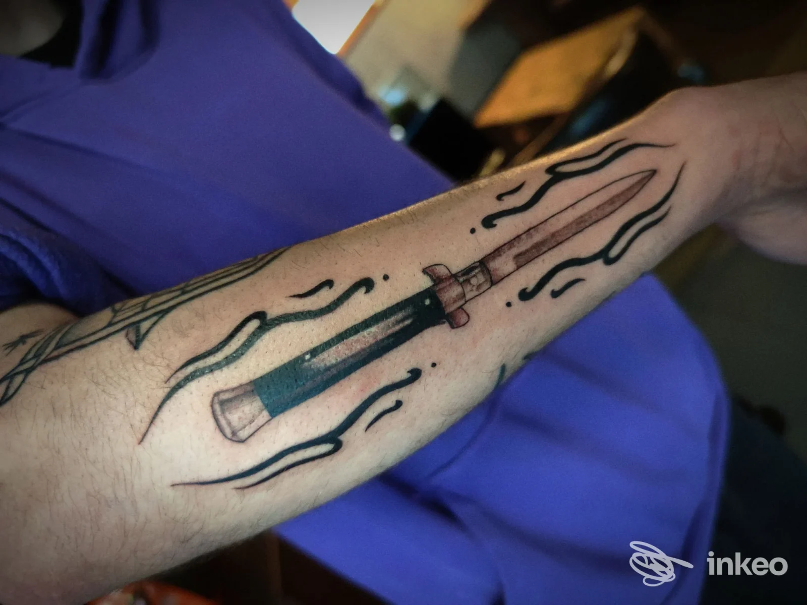 Avambraccio con tatuaggio stilizzato a lama, contorno scuro su pelle, senza volto visibile.
