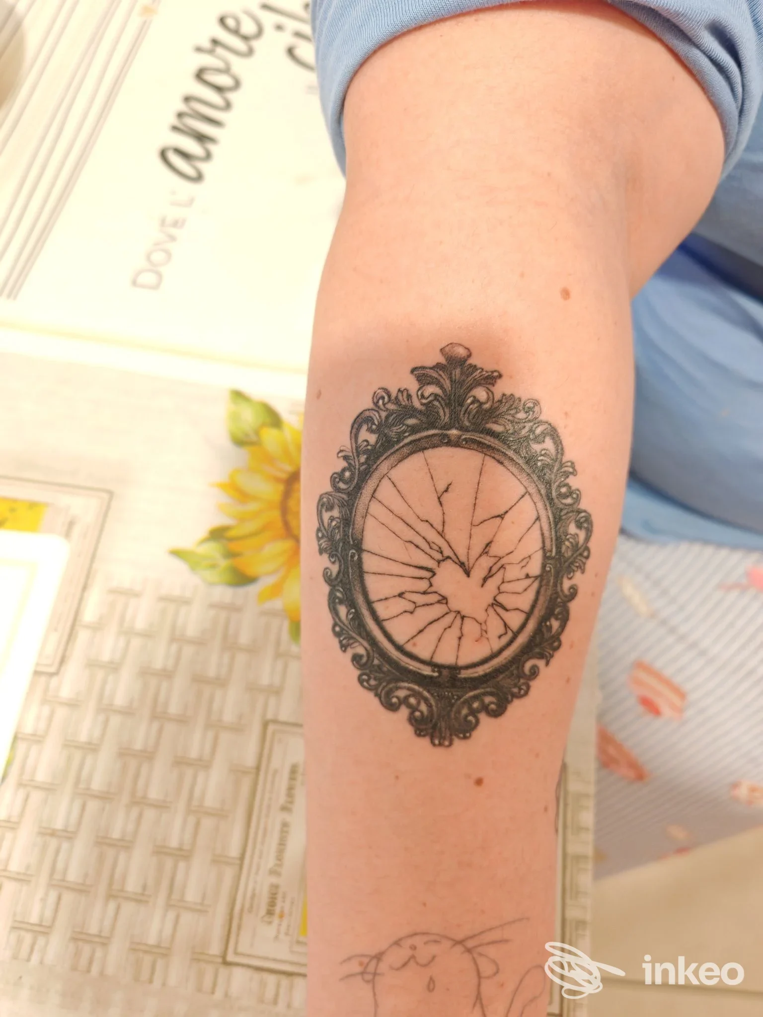 Tattoo su braccio raffigurante un orologio con cornice decorativa, con crepa al centro e linee scure, in stile tradizionale.