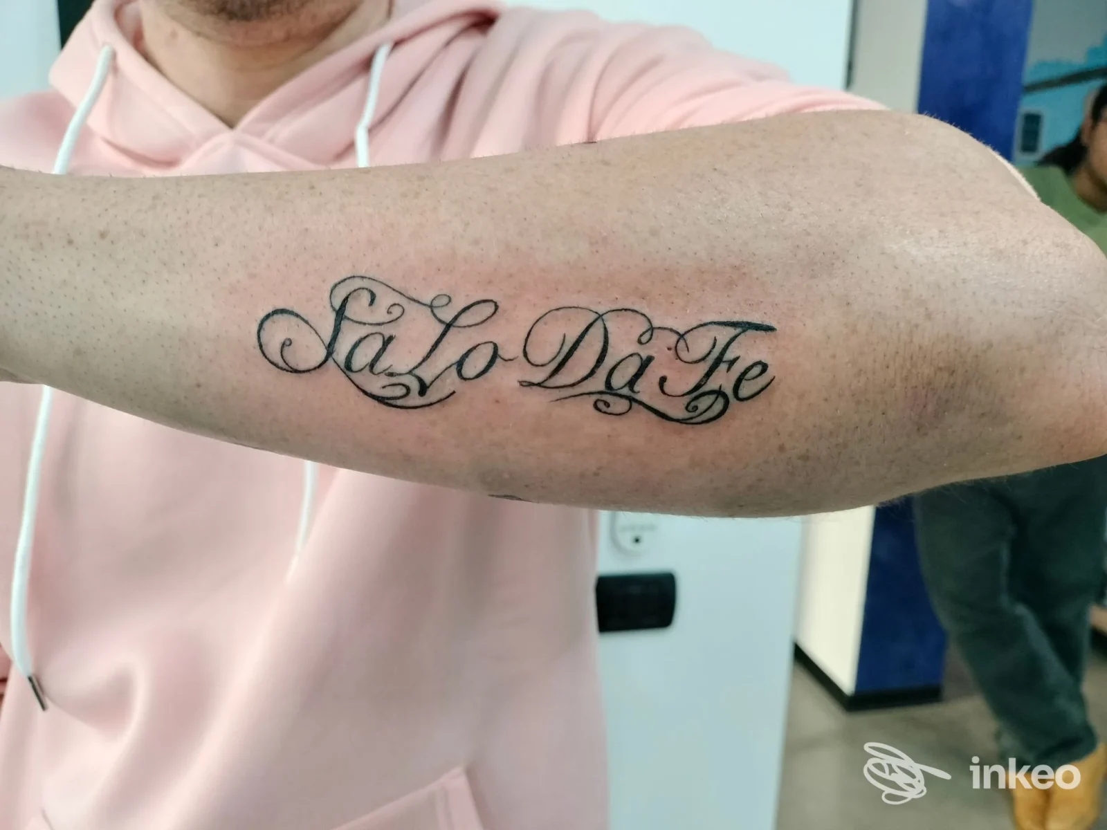 Tatuaggio realizzato sull'avambraccio: scrittura corsiva elegante e decorativa, visibile in primo piano, senza volto o elementi di interfaccia sociale.