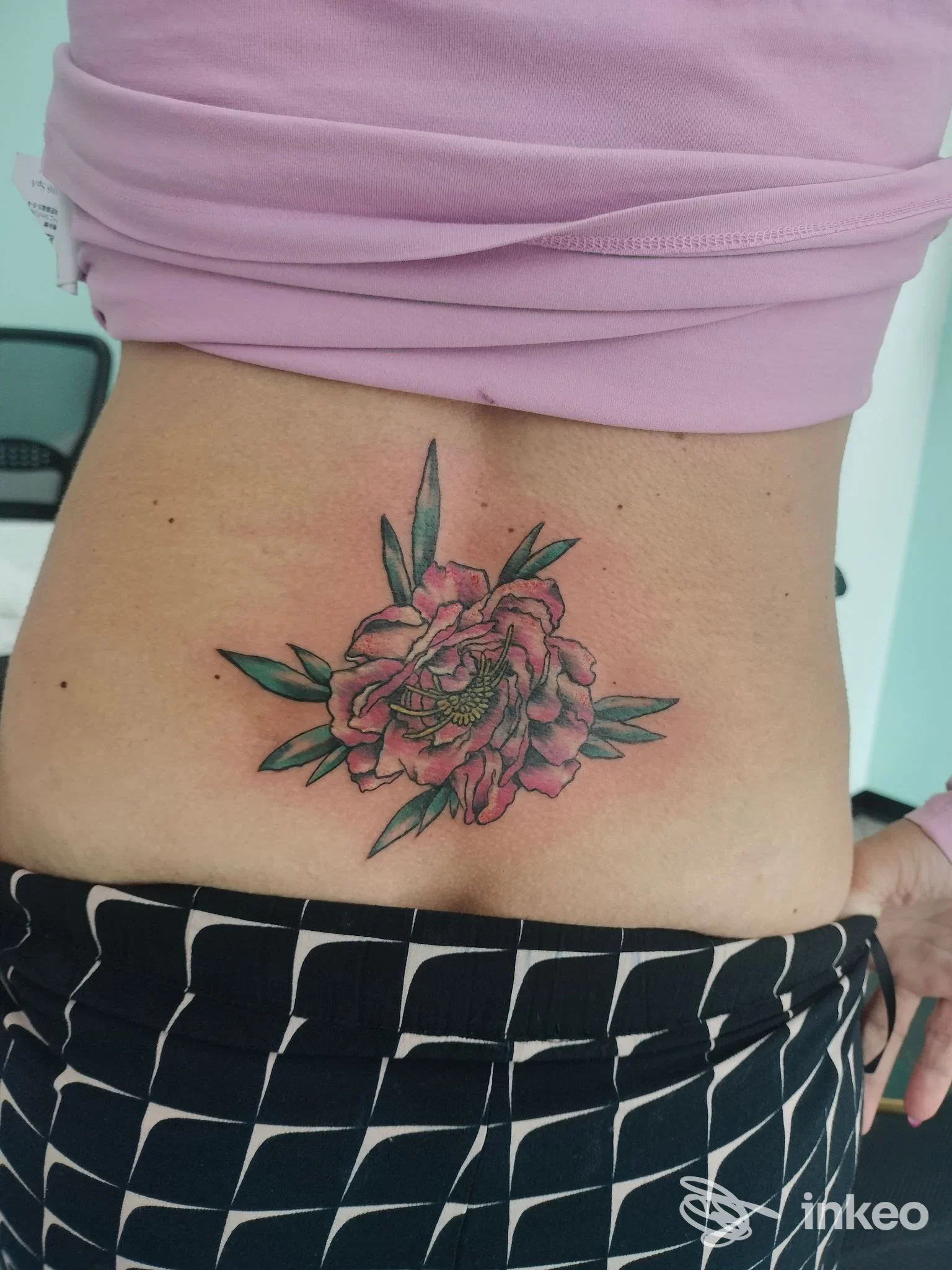 Tattoo colorato di fiore con foglie visibile sulla zona lombare, realizzato dallo studio Tawtoo.