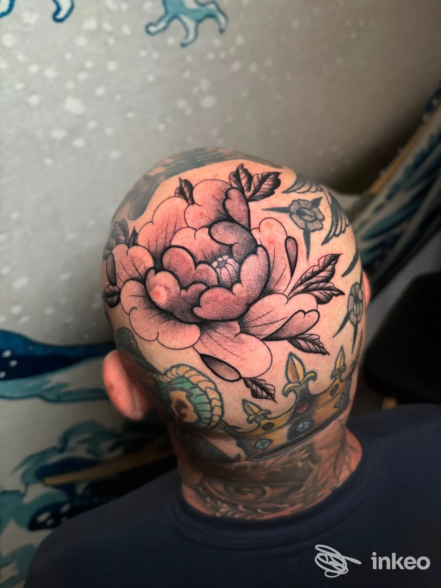 Testa tagliata dall’alto con un grande tatuaggio floreale rosa sulla nuca e sulla sommità della testa, visibile solo parzialmente la faccia.