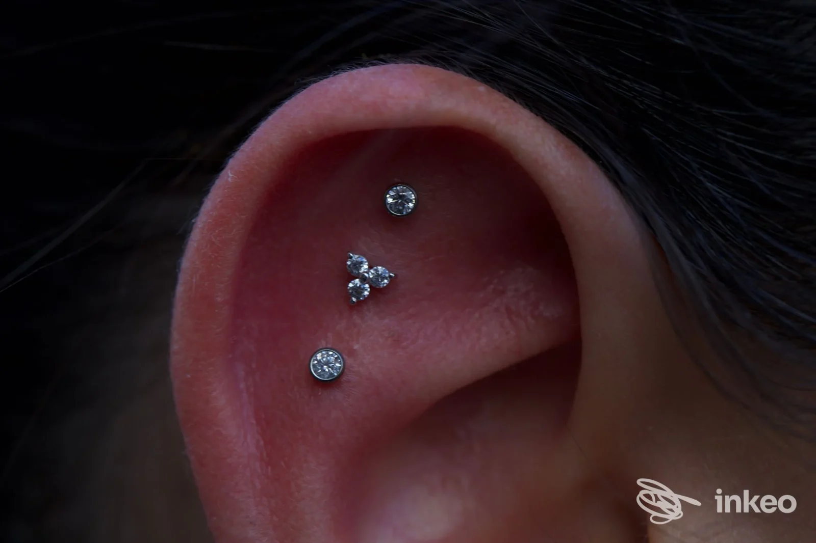 Orecchio umano con piercing multipli: due gioielli sul lobo e due piercing sull'orecchio superiore, realizzati con piccoli zaffiri o pietre, visibili da vicino.